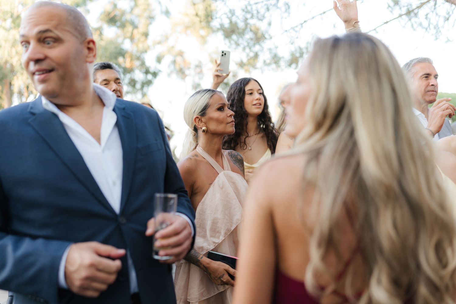Wedding guests mingling and dancing at outdoor celebration during golden hour.