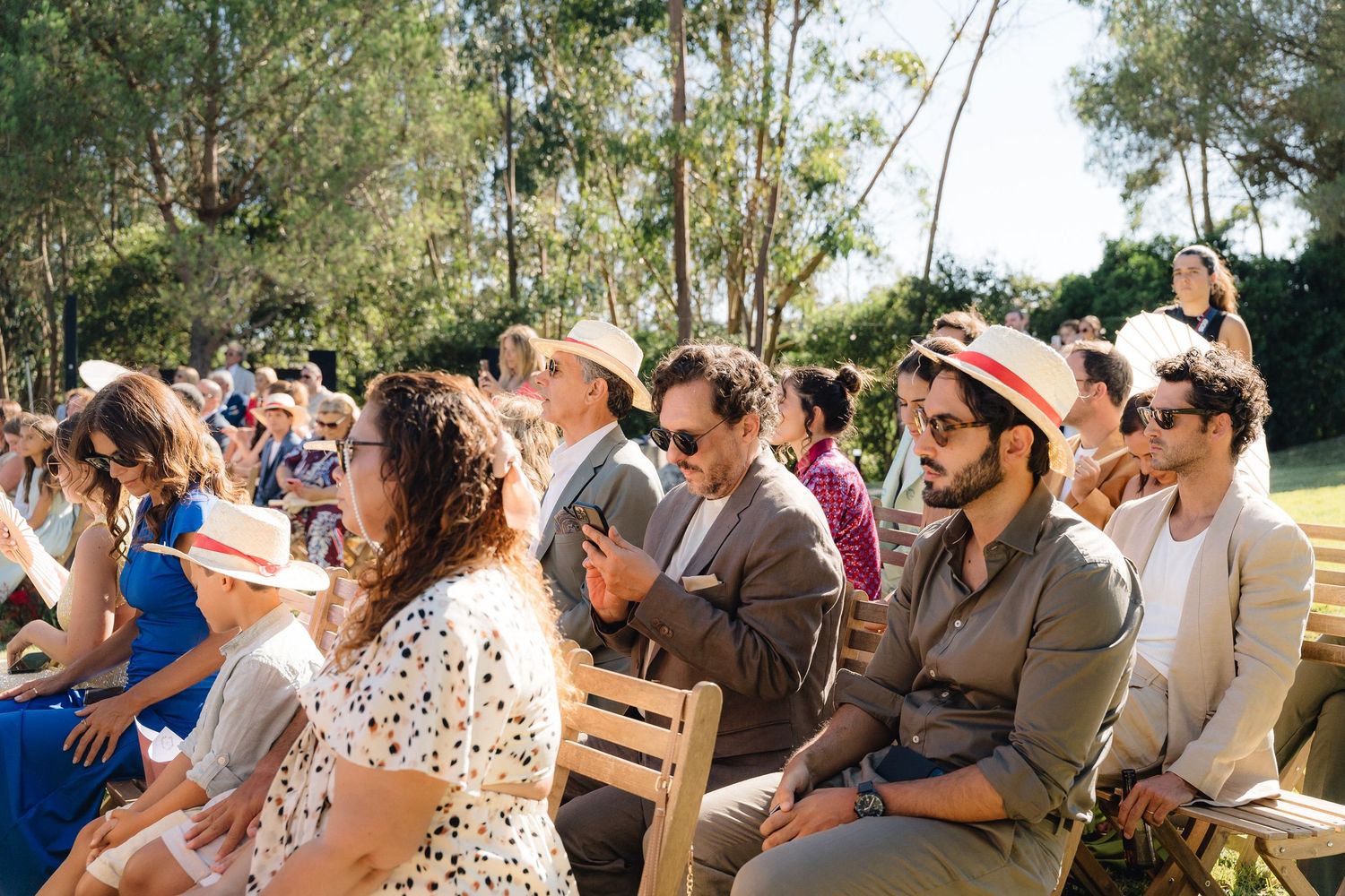 Wedding guests seated in rows watching emotional ceremony under bright sunlight.