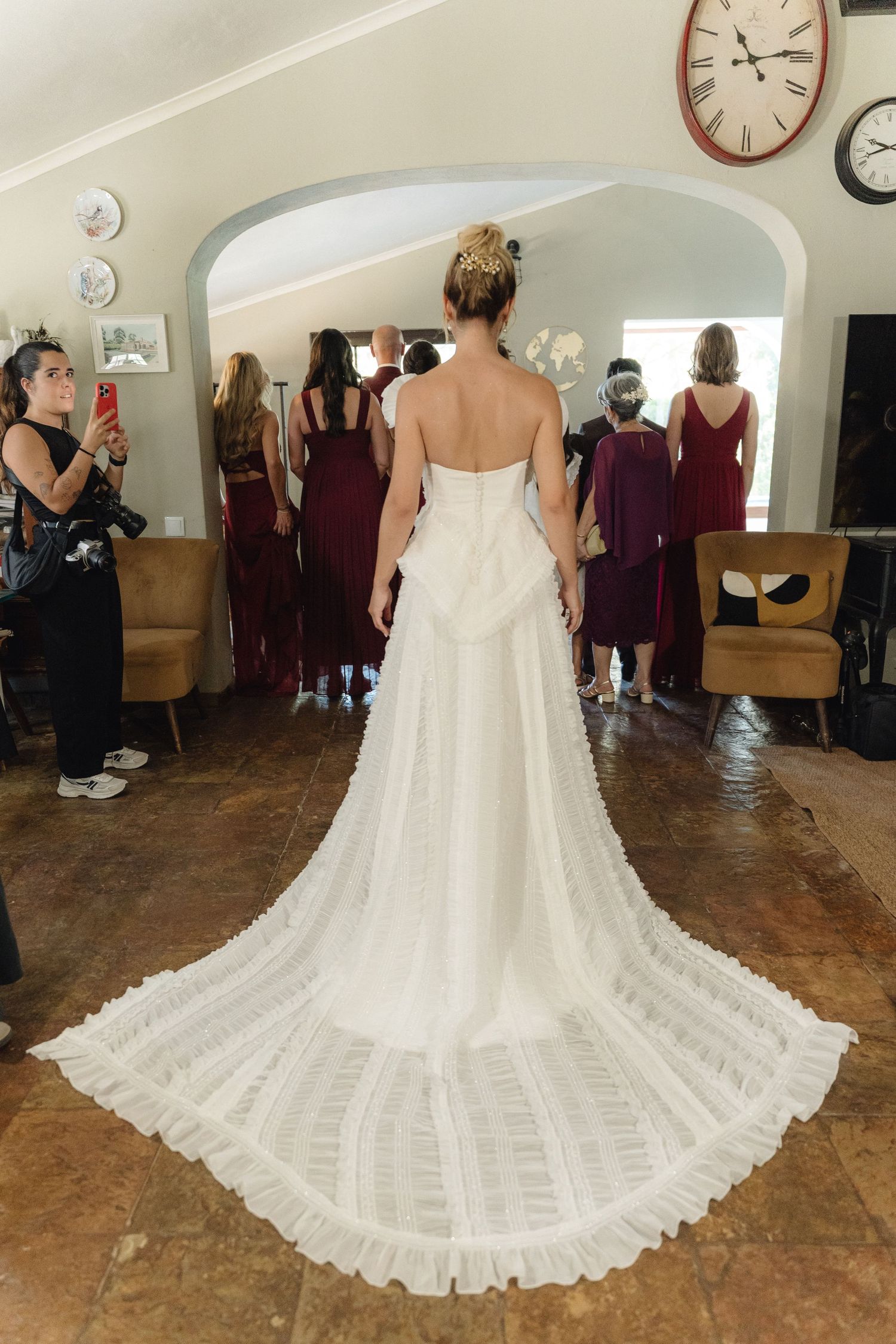Back view of a flowing white wedding dress with intricate pleated train on tile floor.