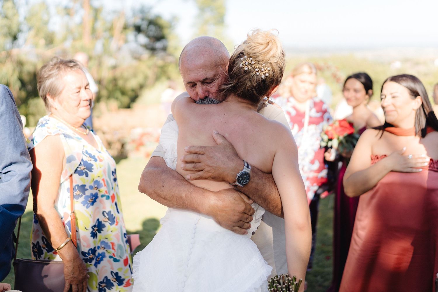 Candid moments of guests hugging during a sunny outdoor wedding reception.