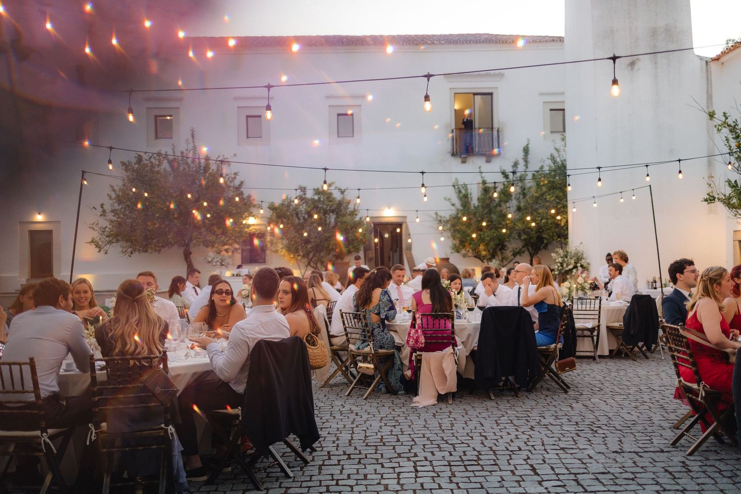 Outdoor evening reception with string lights and white walls creating a romantic atmosphere.