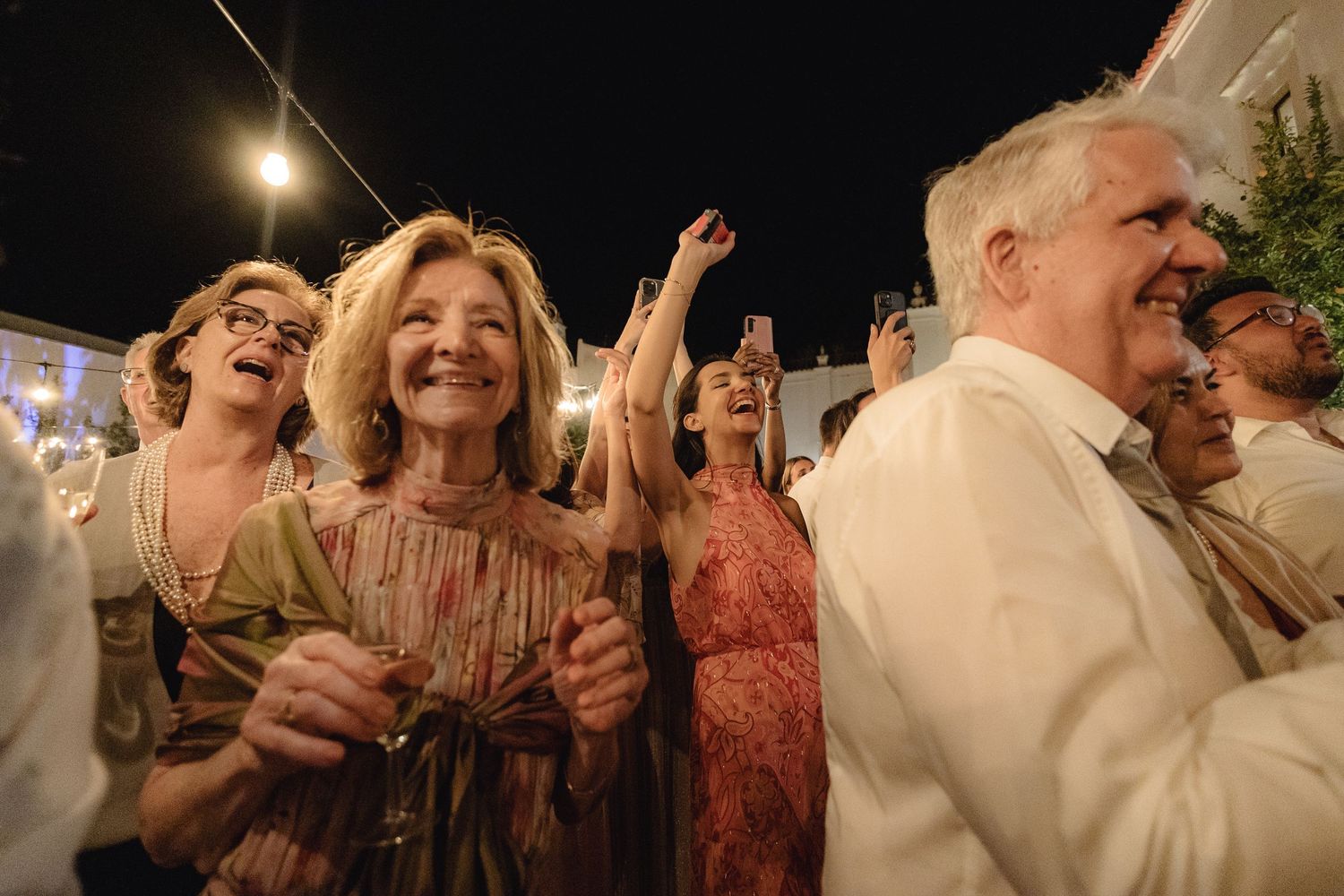 Guests dancing and celebrating under twinkling lights at an outdoor evening wedding reception.