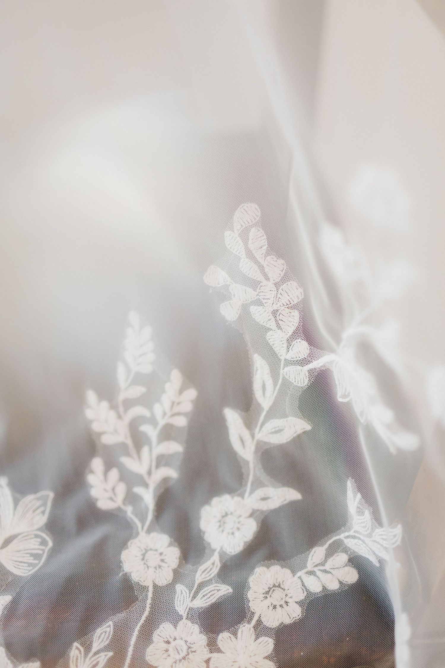 Delicate white lace floral embroidery detail on wedding veil fabric.