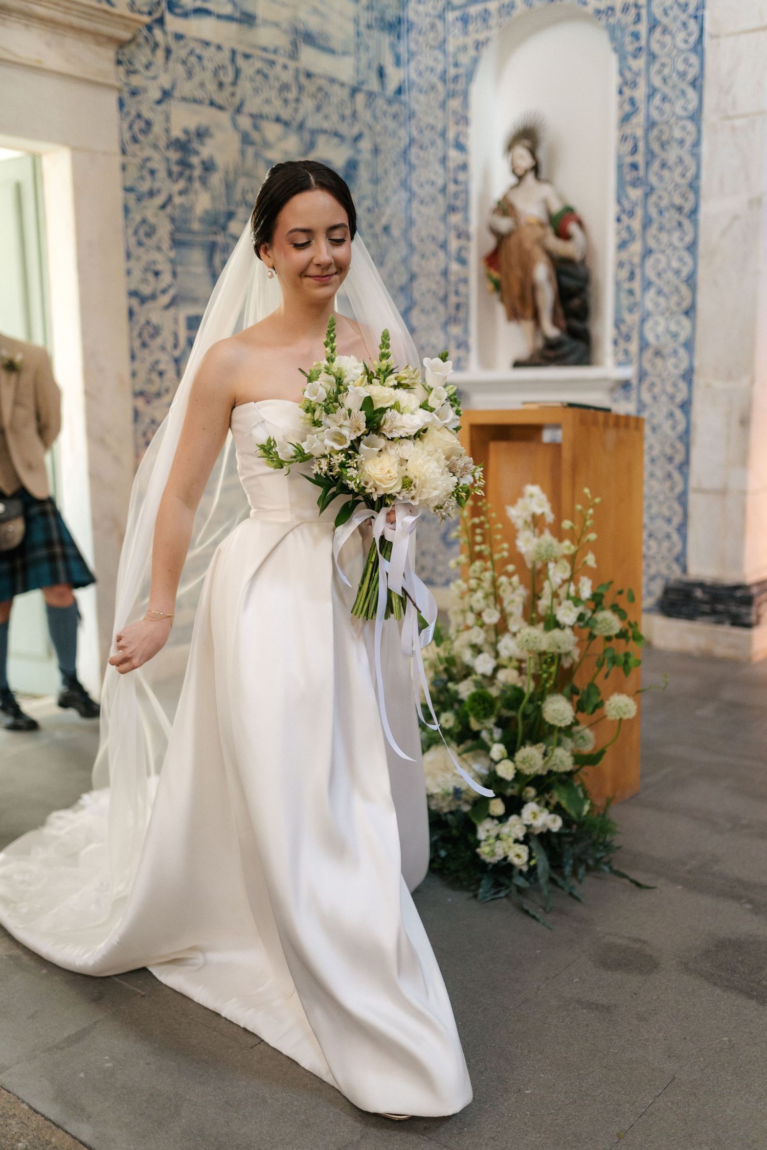 Elegant white wedding dress with flowing train against blue tiled church interior.