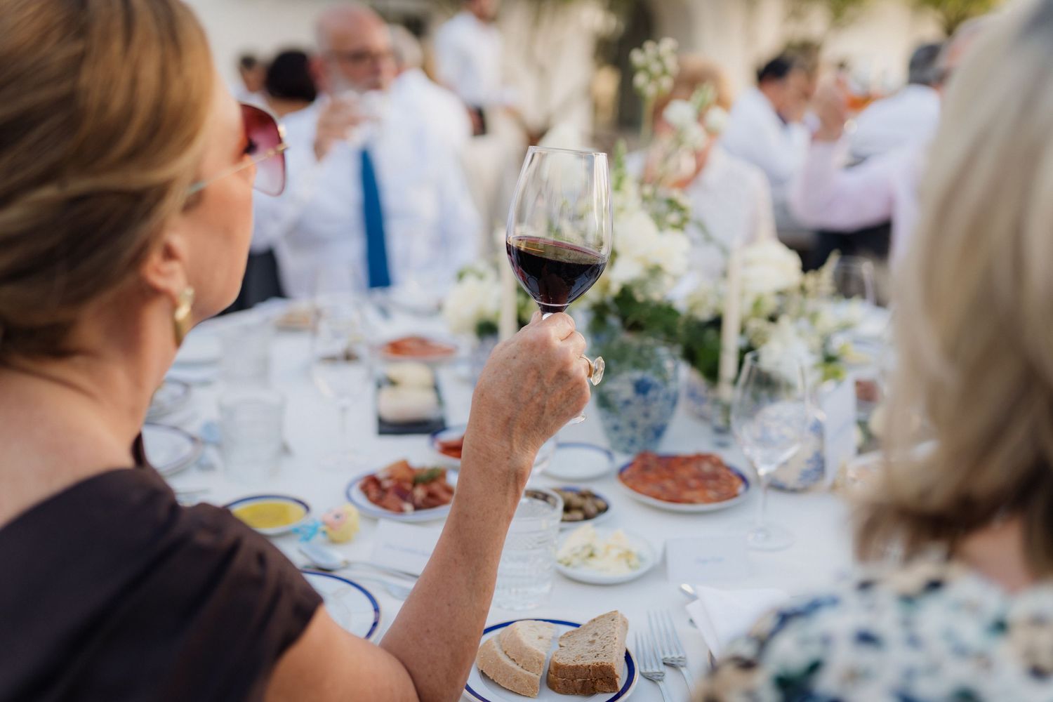 Diners raise their wine glasses in a toast at an elegant outdoor gathering.