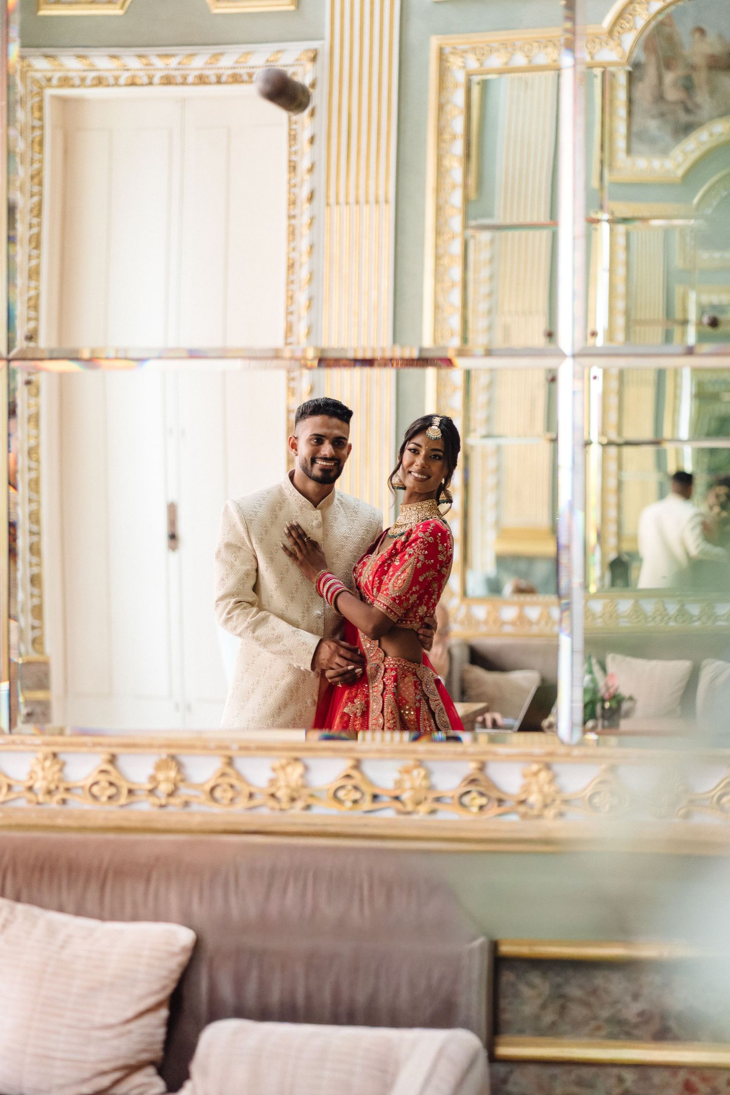 Reflection of couple in ornate mirror wearing traditional Indian wedding attire.