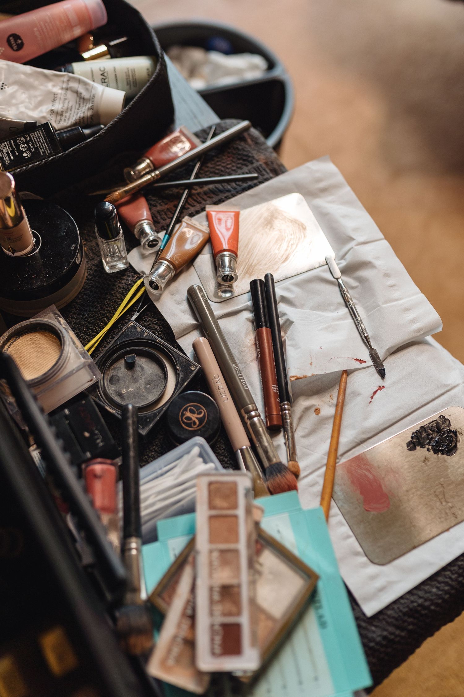 Makeup products and cosmetics scattered on a turquoise surface including brushes and palettes.