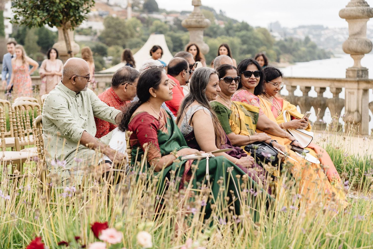Wedding celebration guests seated outdoors in front of historic building with mountain backdrop.