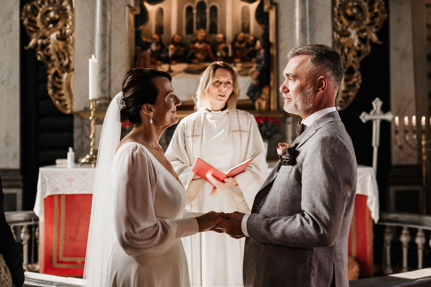 A wedding ceremony takes place in a historic church with ornate gold details and candlelit altar.