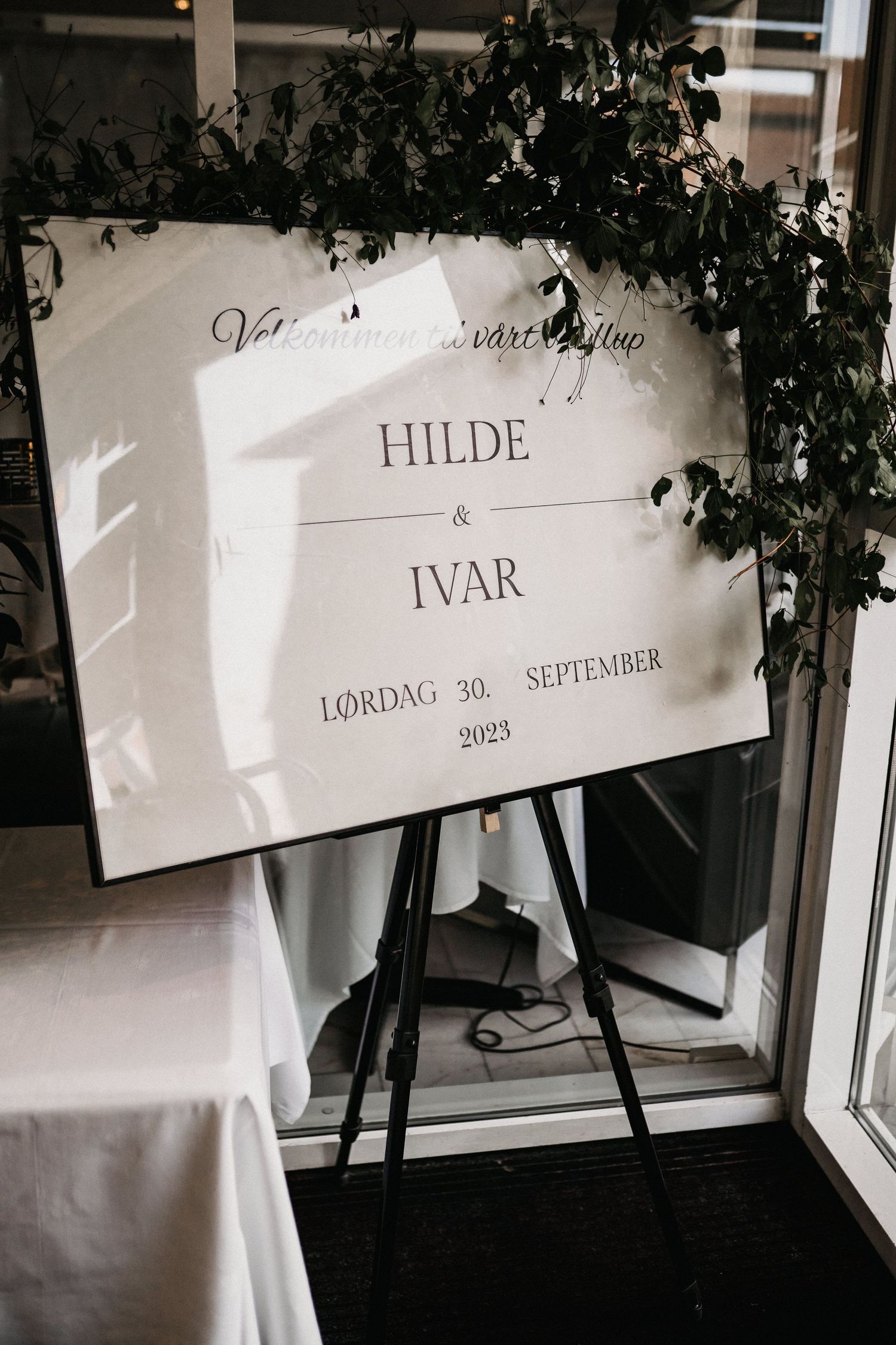 Wedding signage with names and date displayed against a light background with greenery.
