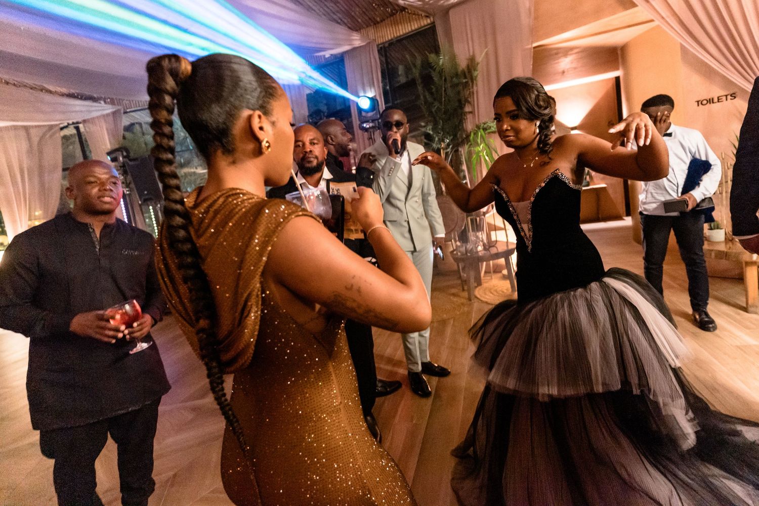 Wedding guests dancing and celebrating under decorative lighting at an evening reception.