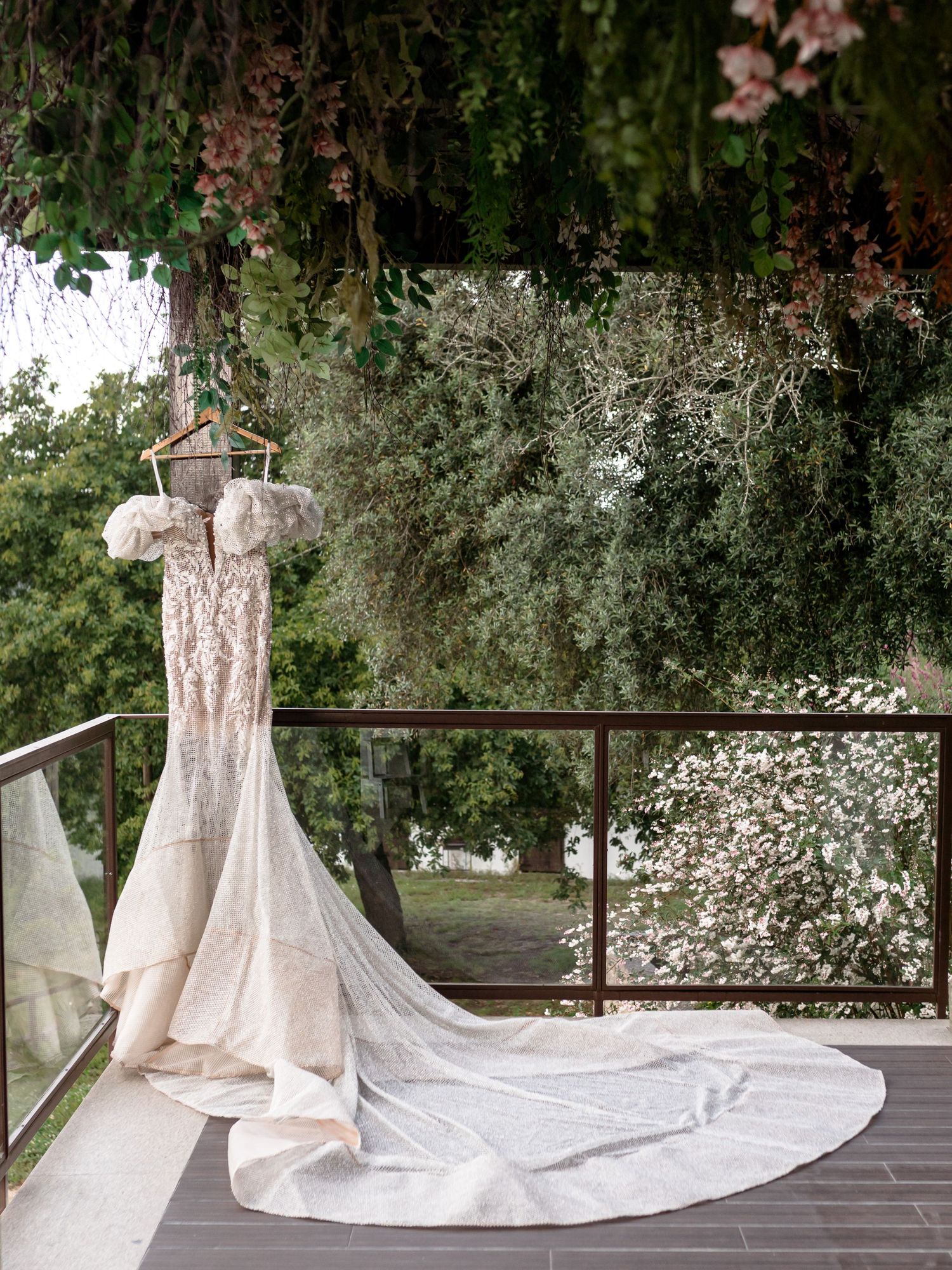 Elegant white wedding dress with long train displayed outdoors on stone patio.