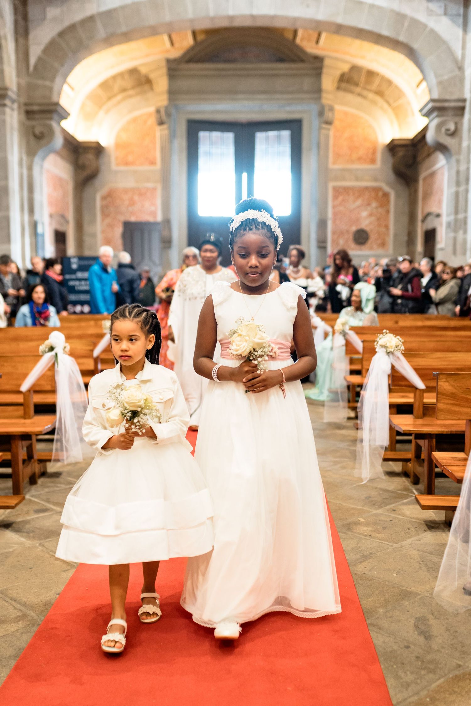 Wedding ceremony processional in historic church with red carpet and ornate architecture.