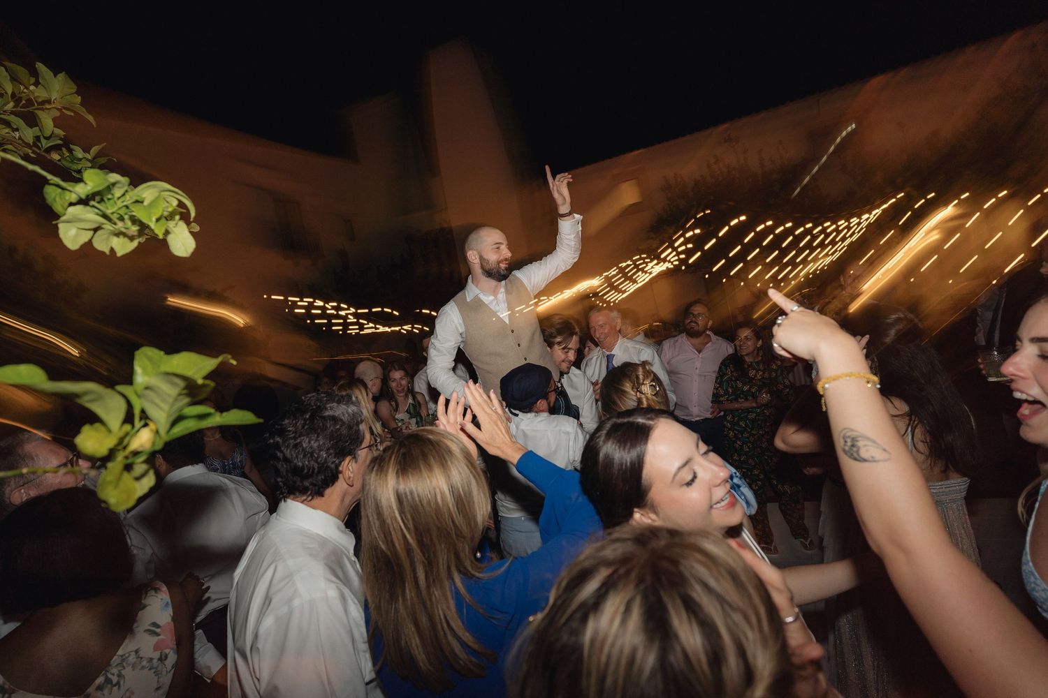 Crowded dance floor with guests celebrating under string lights at an outdoor venue.