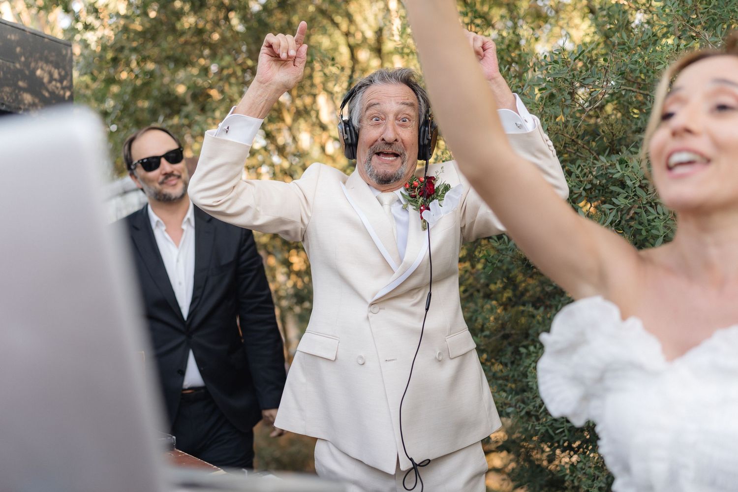 Wedding DJ performing at an outdoor celebration with music equipment and trees in background.