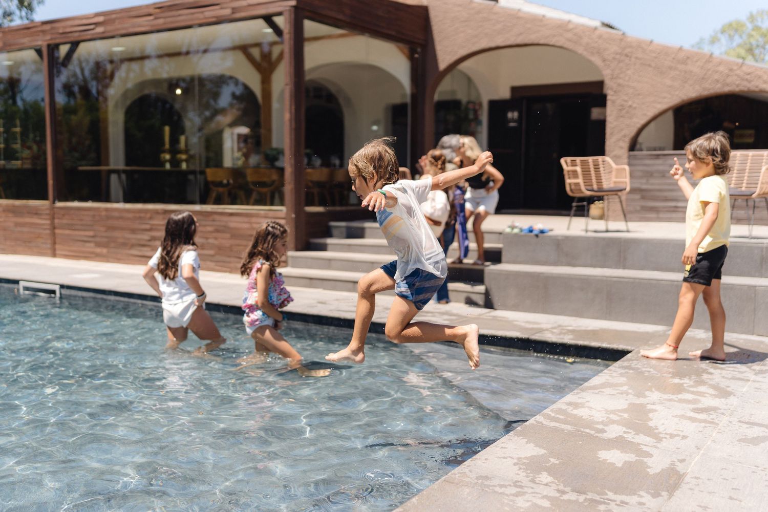 Children playing and splashing in a shallow pool on a sunny day.