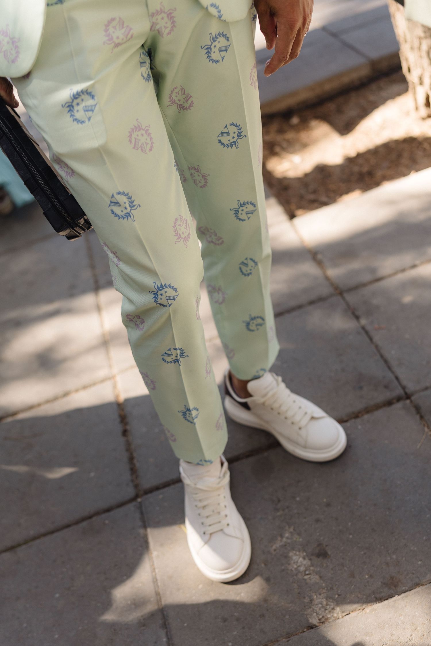 Light mint green pants with cute cartoon print and white sneakers on stone pavement.