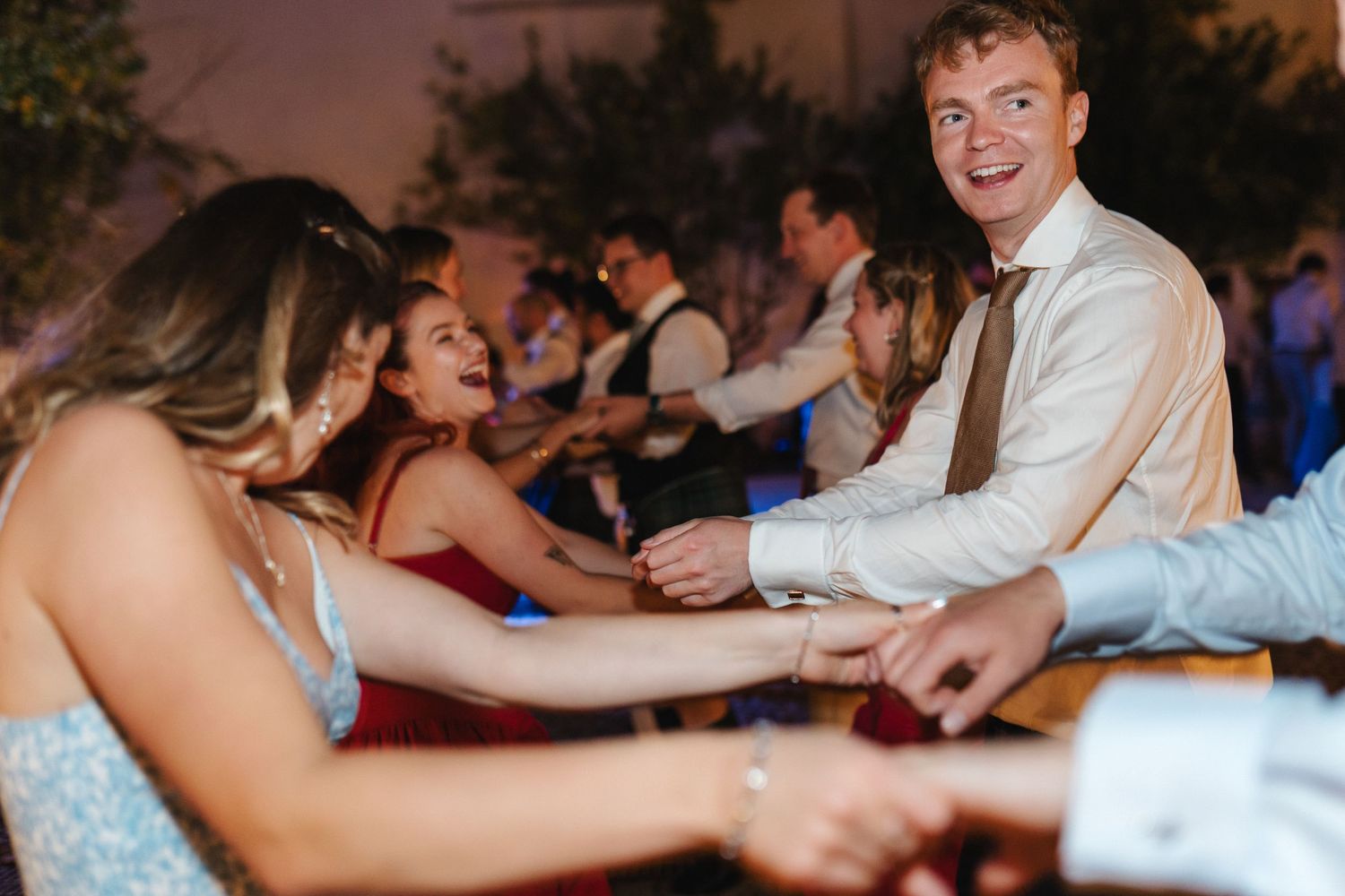 Wedding guests dancing in a line formation during an evening celebration.