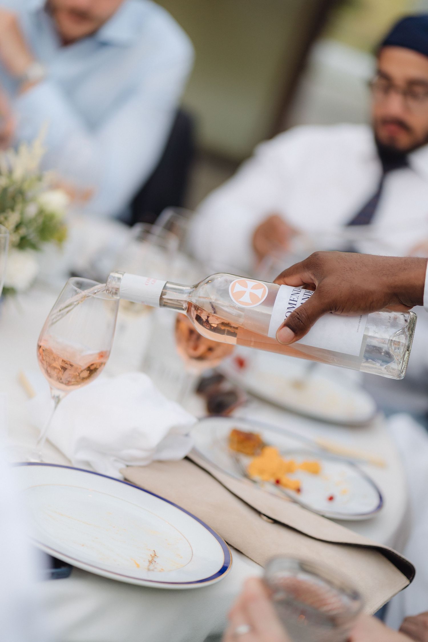 Table setting with white plates and glassware being served at an outdoor dining event.