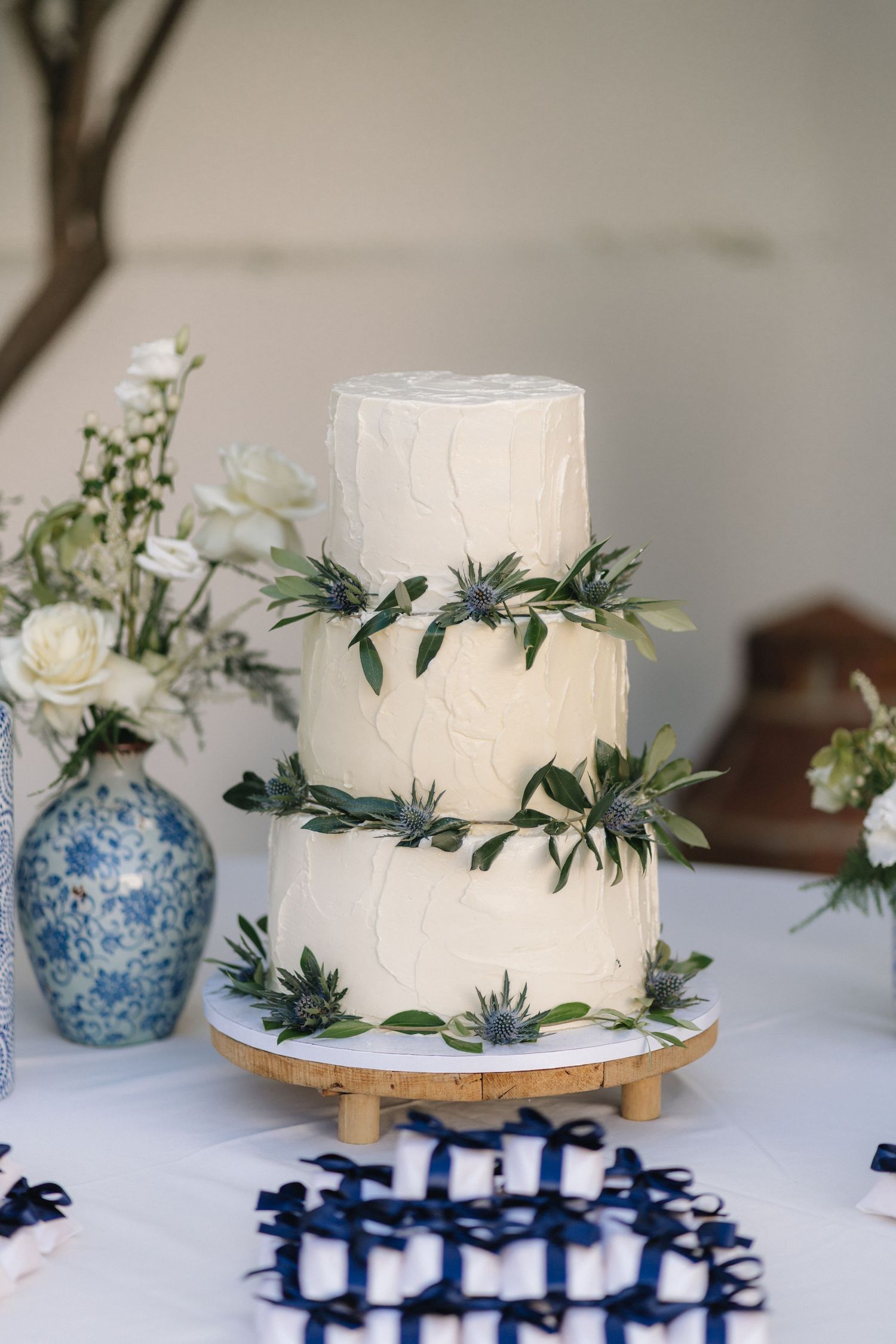 Simple white wedding cake decorated with fresh greenery and eucalyptus leaves on a white tablecloth.