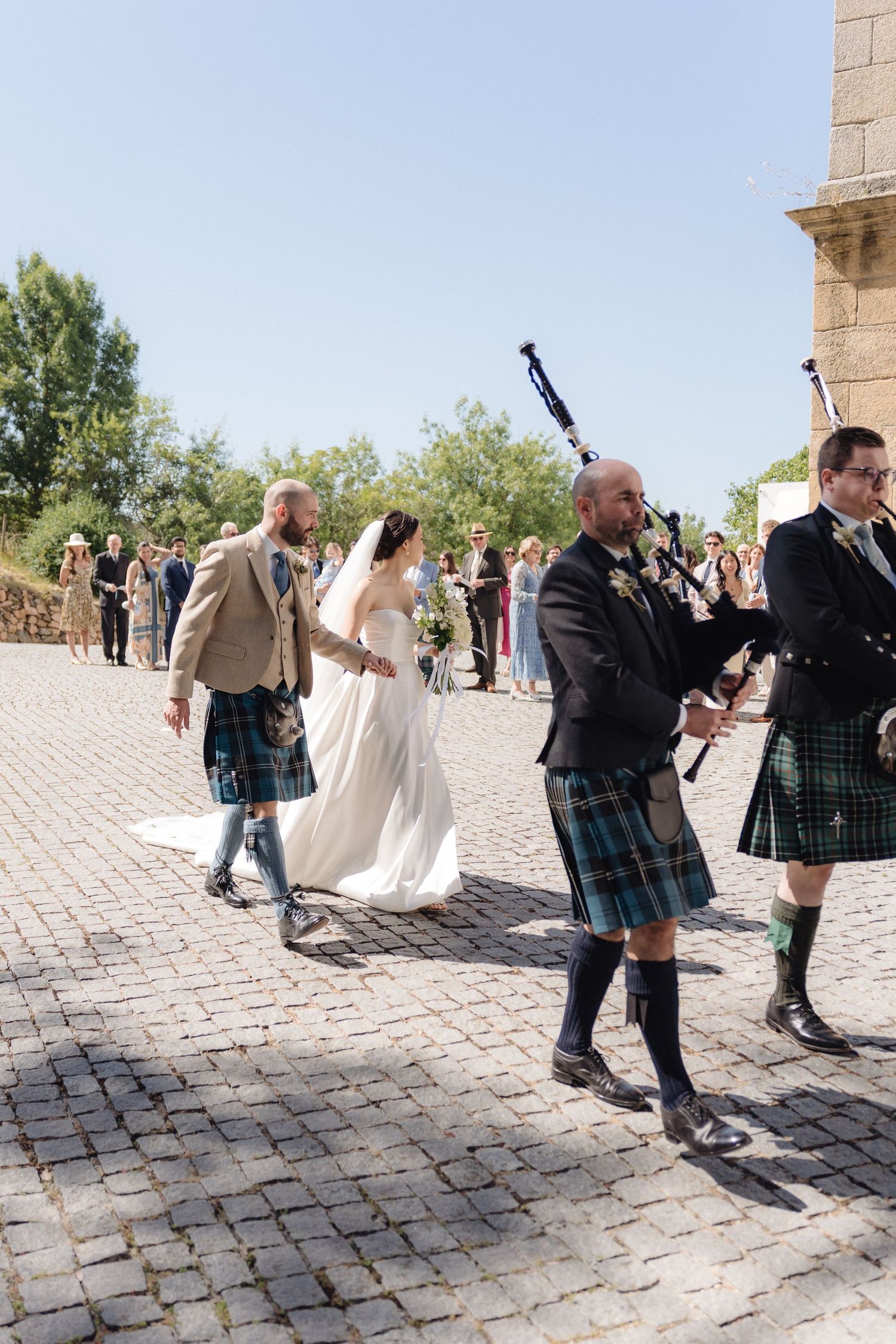 Bagpipers in traditional kilts perform during an outdoor wedding ceremony.