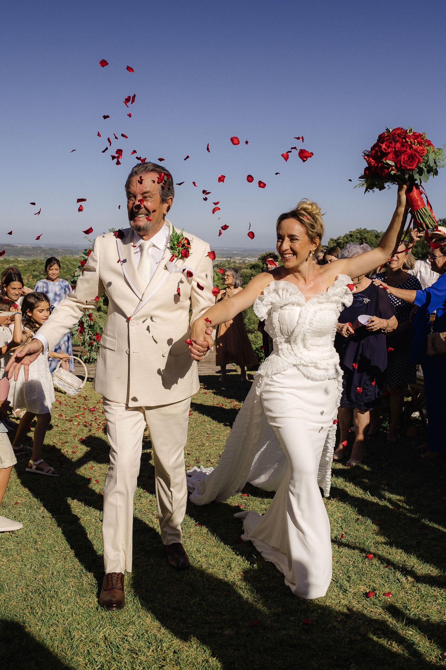 Wedding celebration on sunny lawn with red rose petals being tossed in celebration.