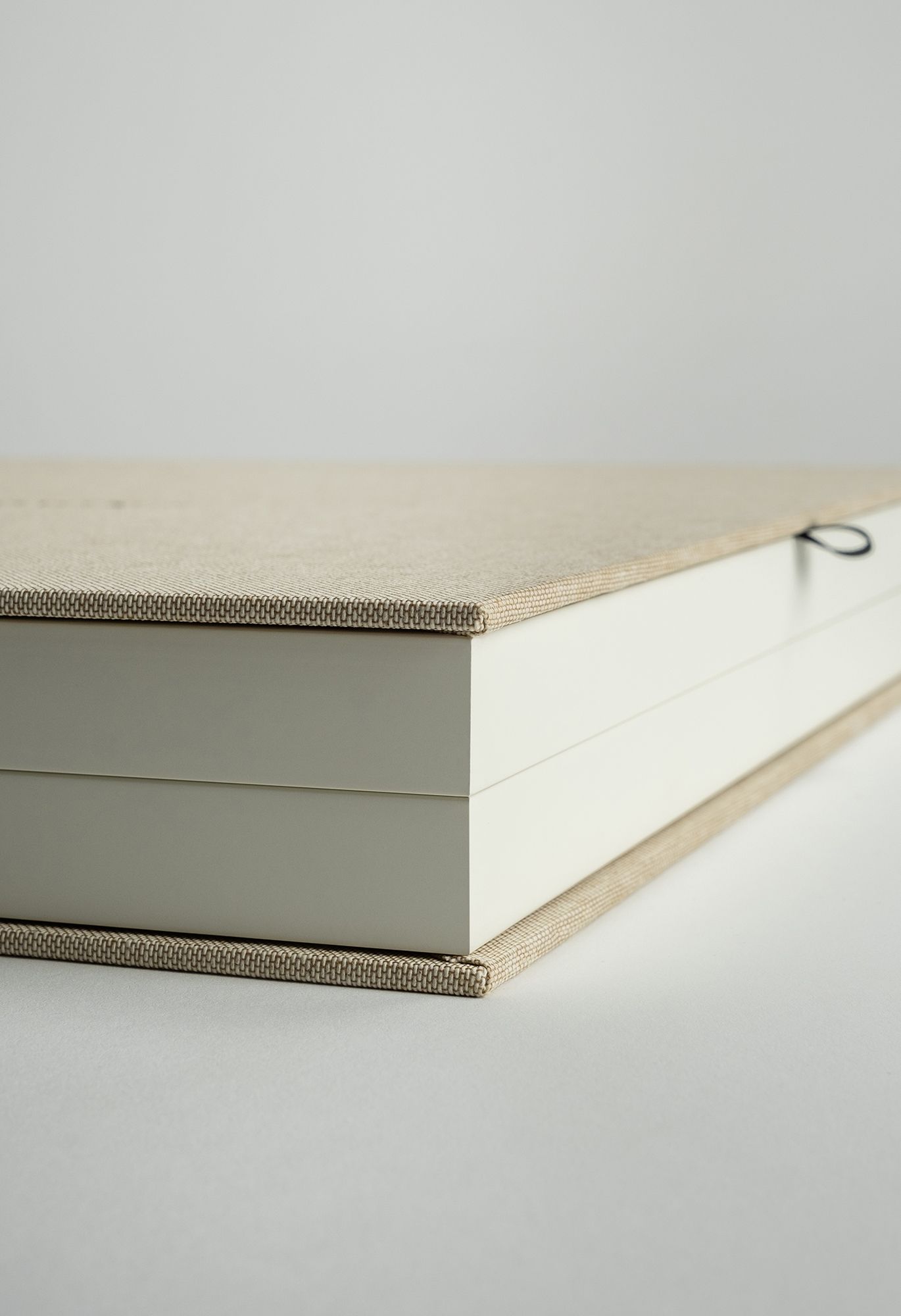 Close-up views of a minimalist book binding process showing cream-colored pages with metallic spine details.
