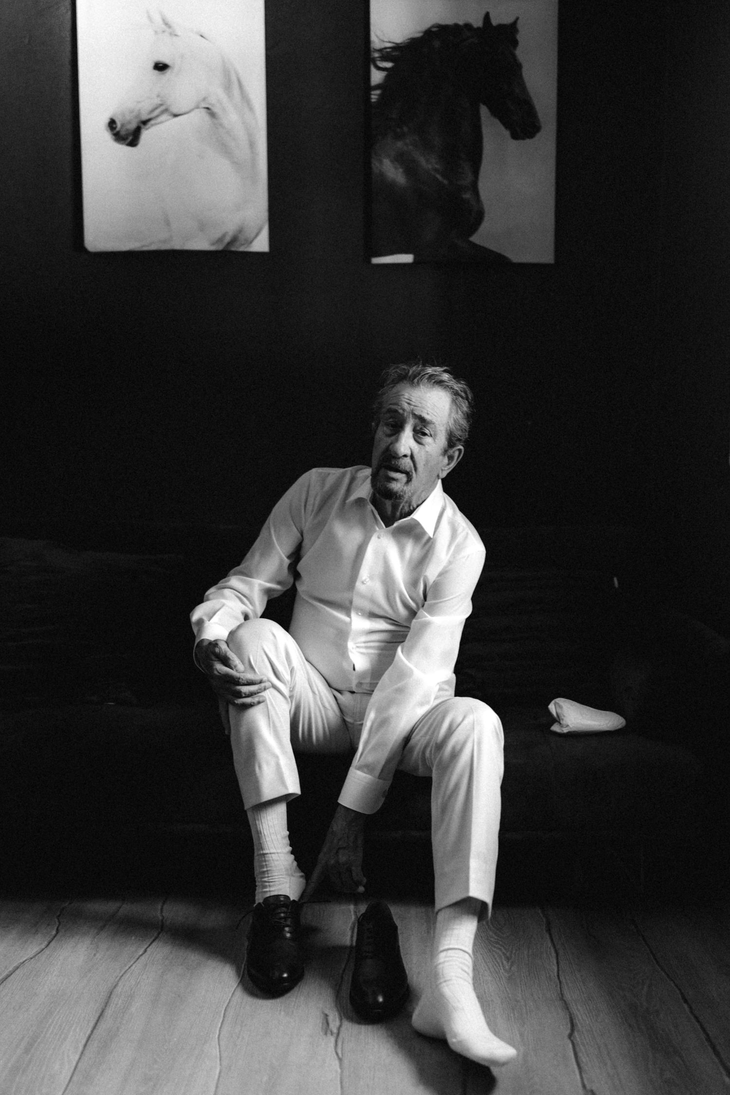 Artistic black and white photos of someone in white clothing sitting on a dark floor.