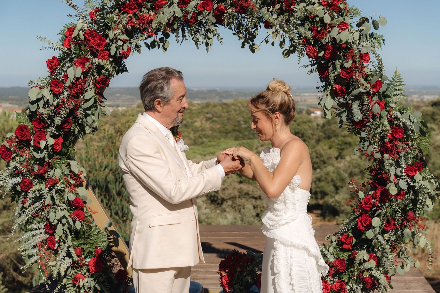 Couple shares a joyful moment under an elegant arch adorned with red roses.