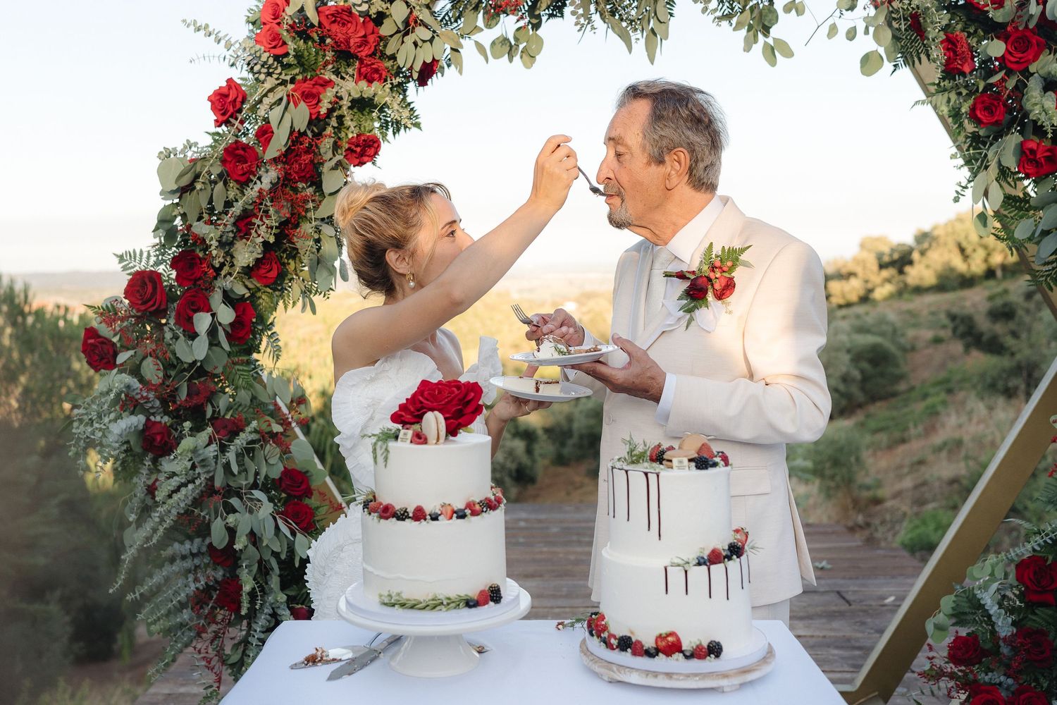 Wedding cake cutting ceremony under an arch decorated with red roses.