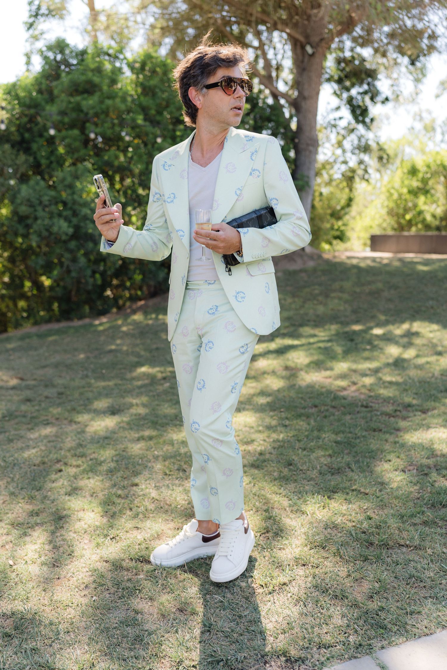 Guest in light mint suit and sneakers poses on grass at outdoor event.