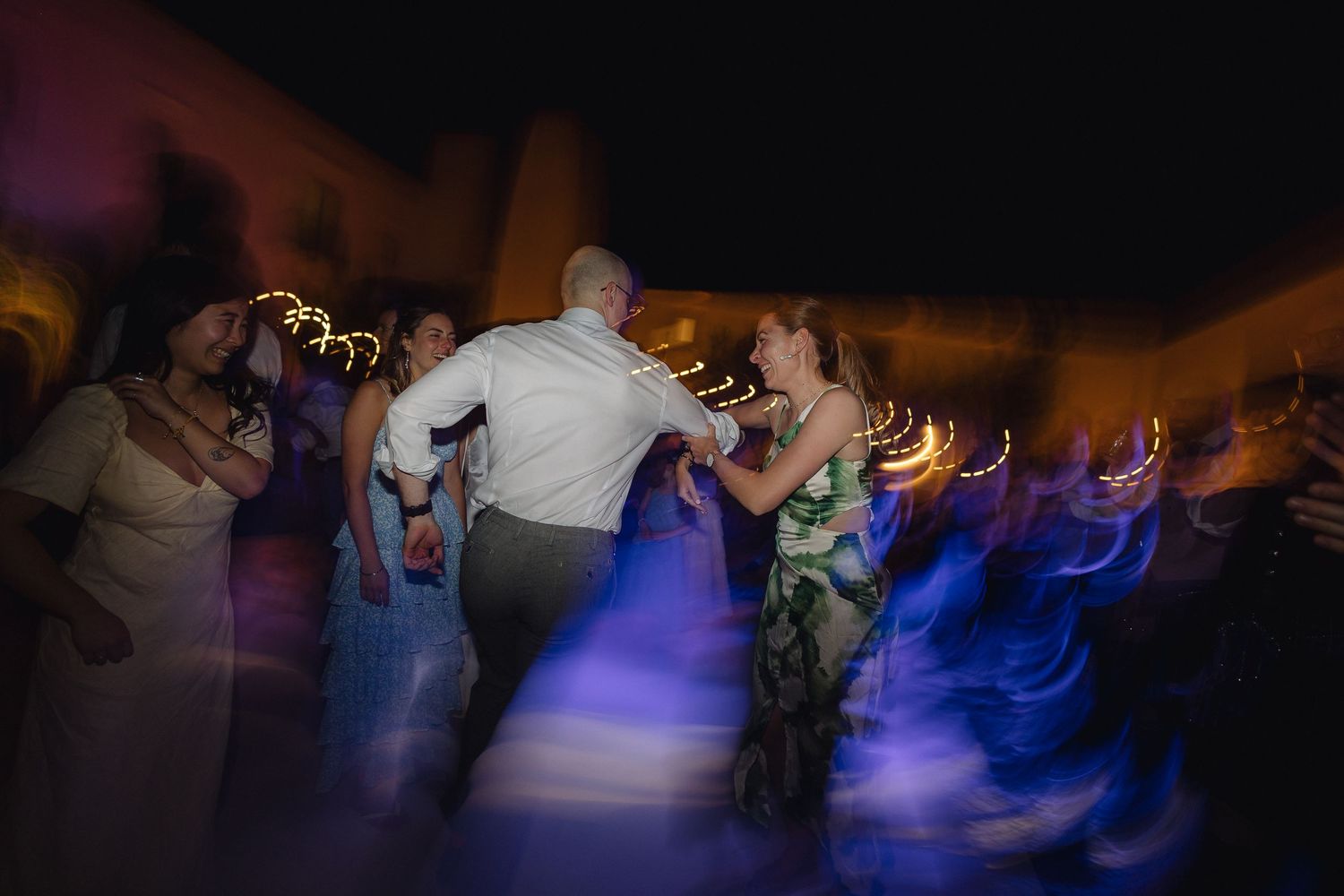 Silhouettes of people dancing at an evening event with purple and blue lighting.