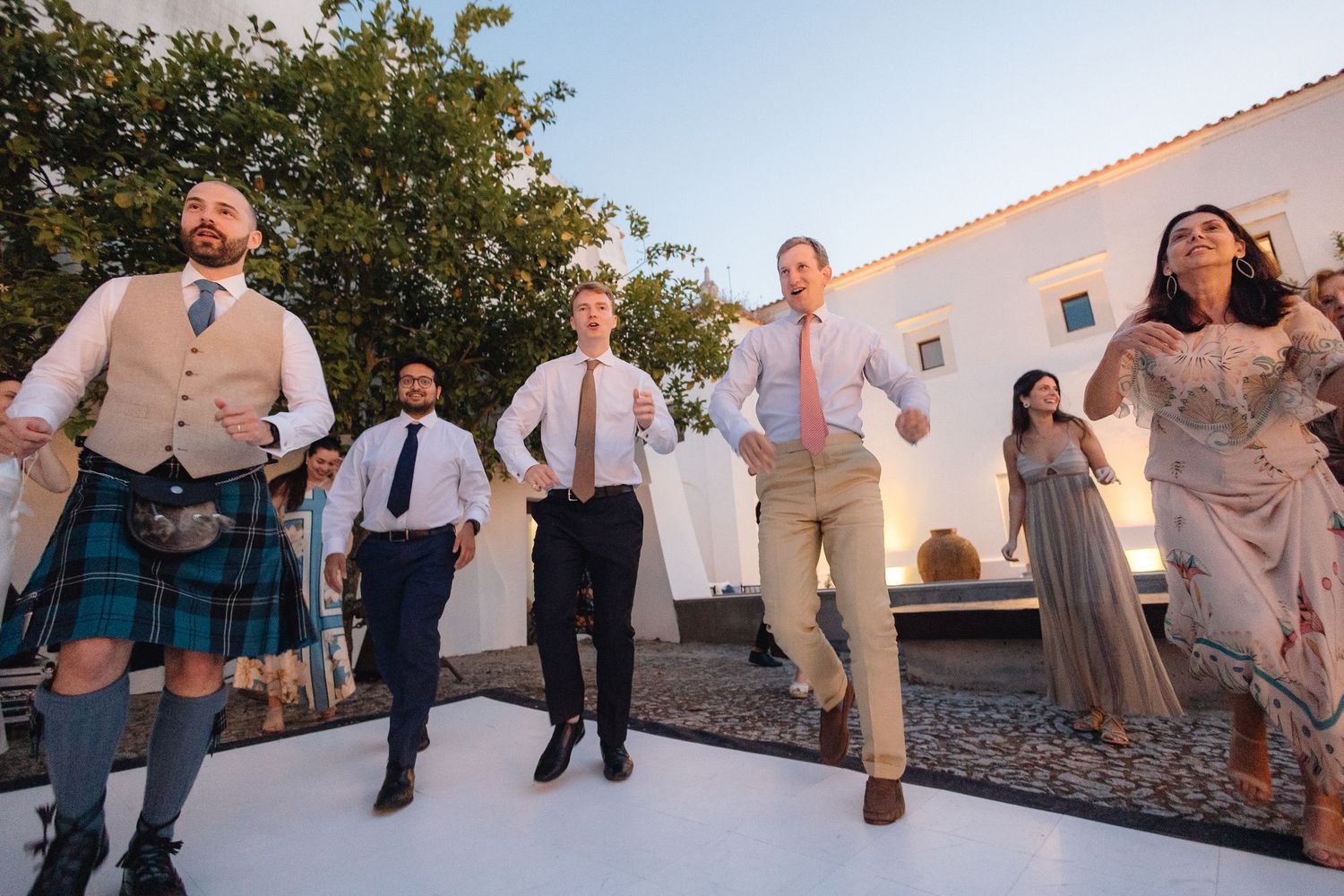 Wedding guests dancing and celebrating in outdoor courtyard venue.