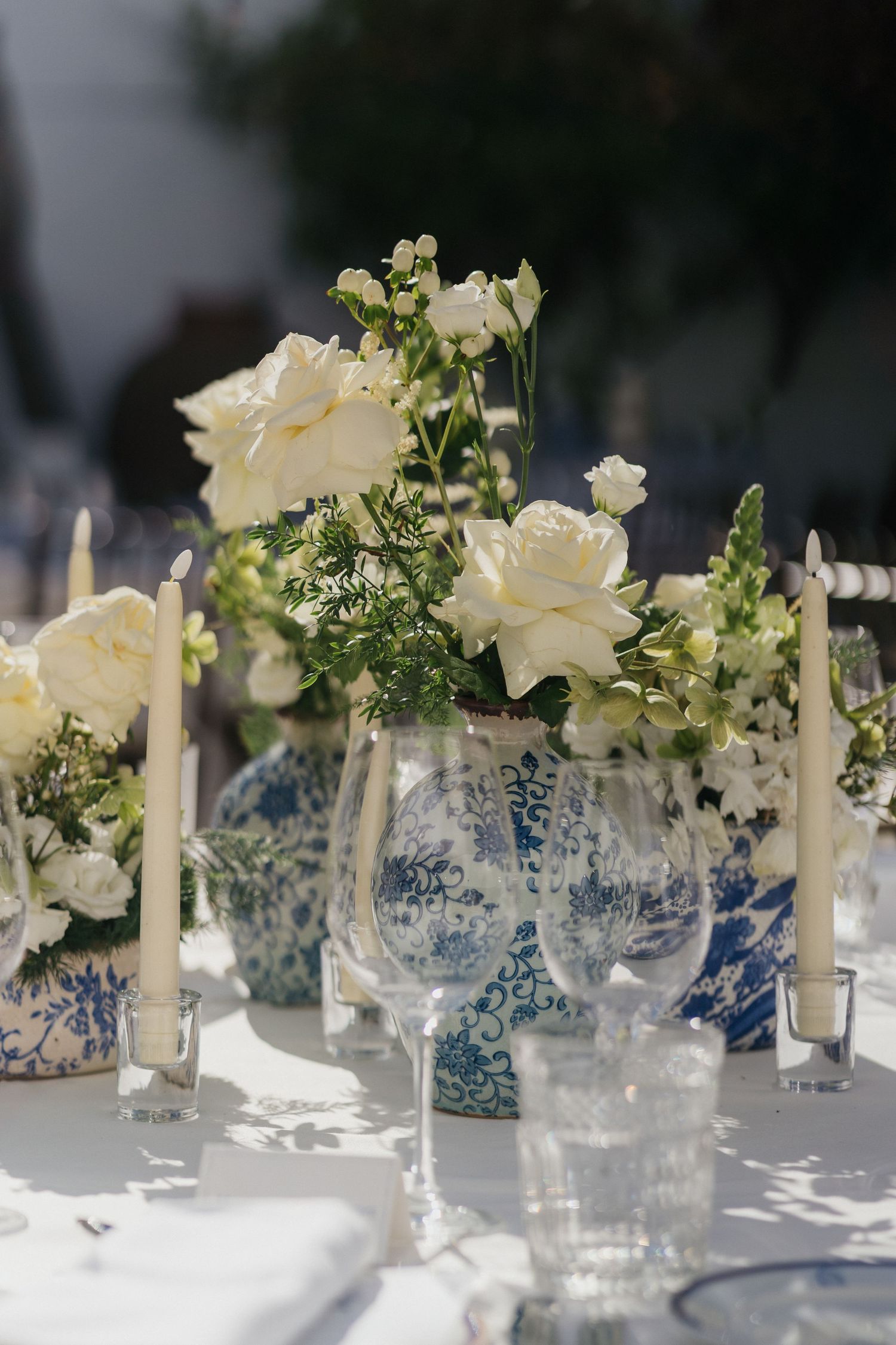 White floral arrangements with blue and white porcelain vases and tall white candles on dining tables.