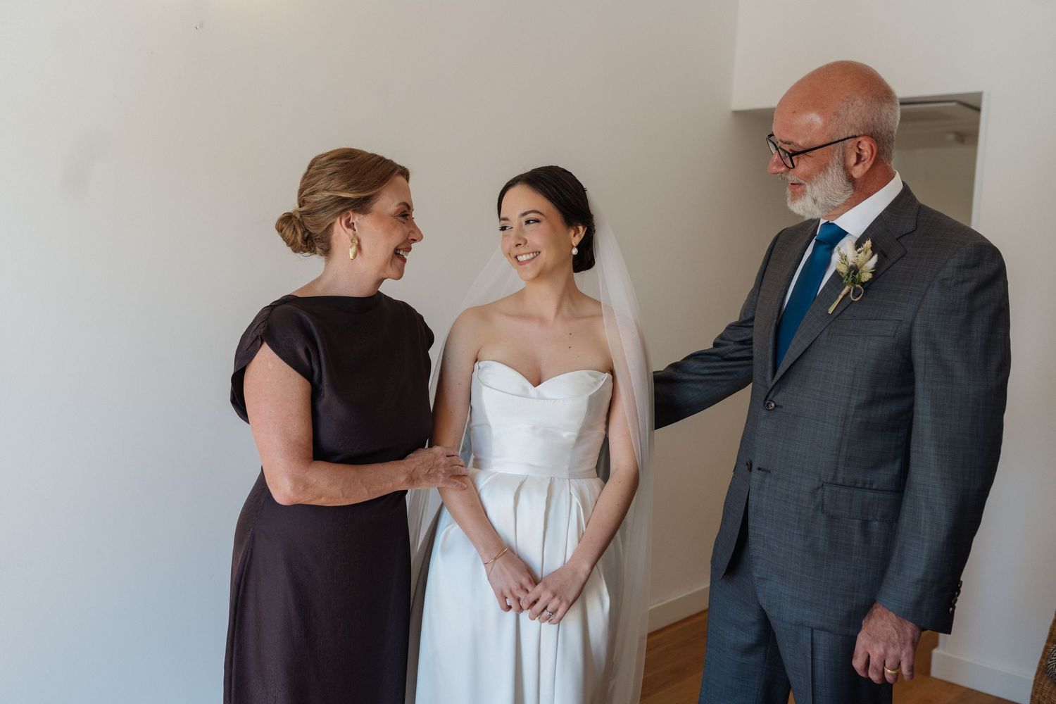 Wedding preparation scene with bride in white dress surrounded by family members.