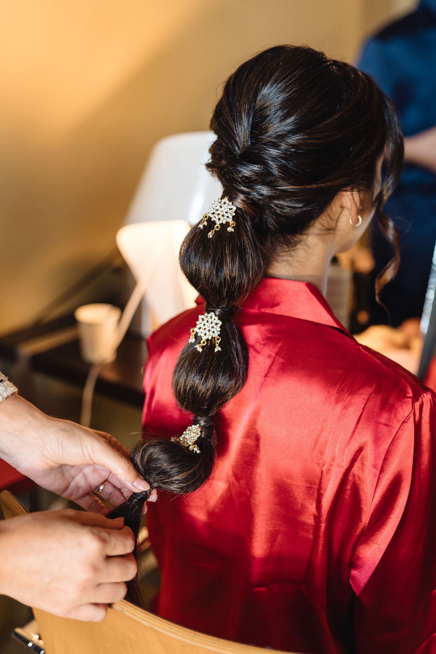 Hands styling dark hair with ornate hair accessories against a red silk robe background.