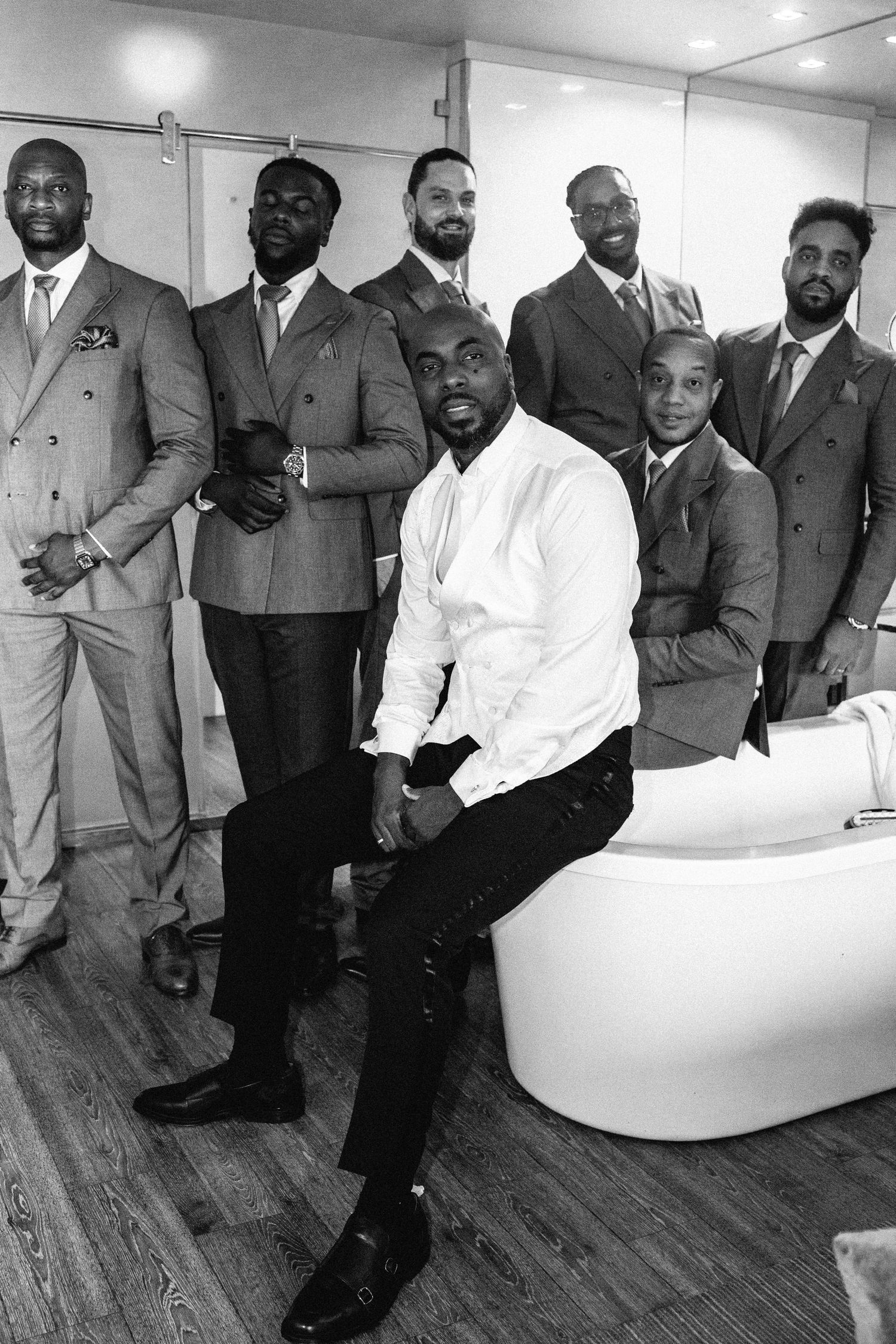 Groomsmen in gray suits and white shirts posing together on wooden floors.