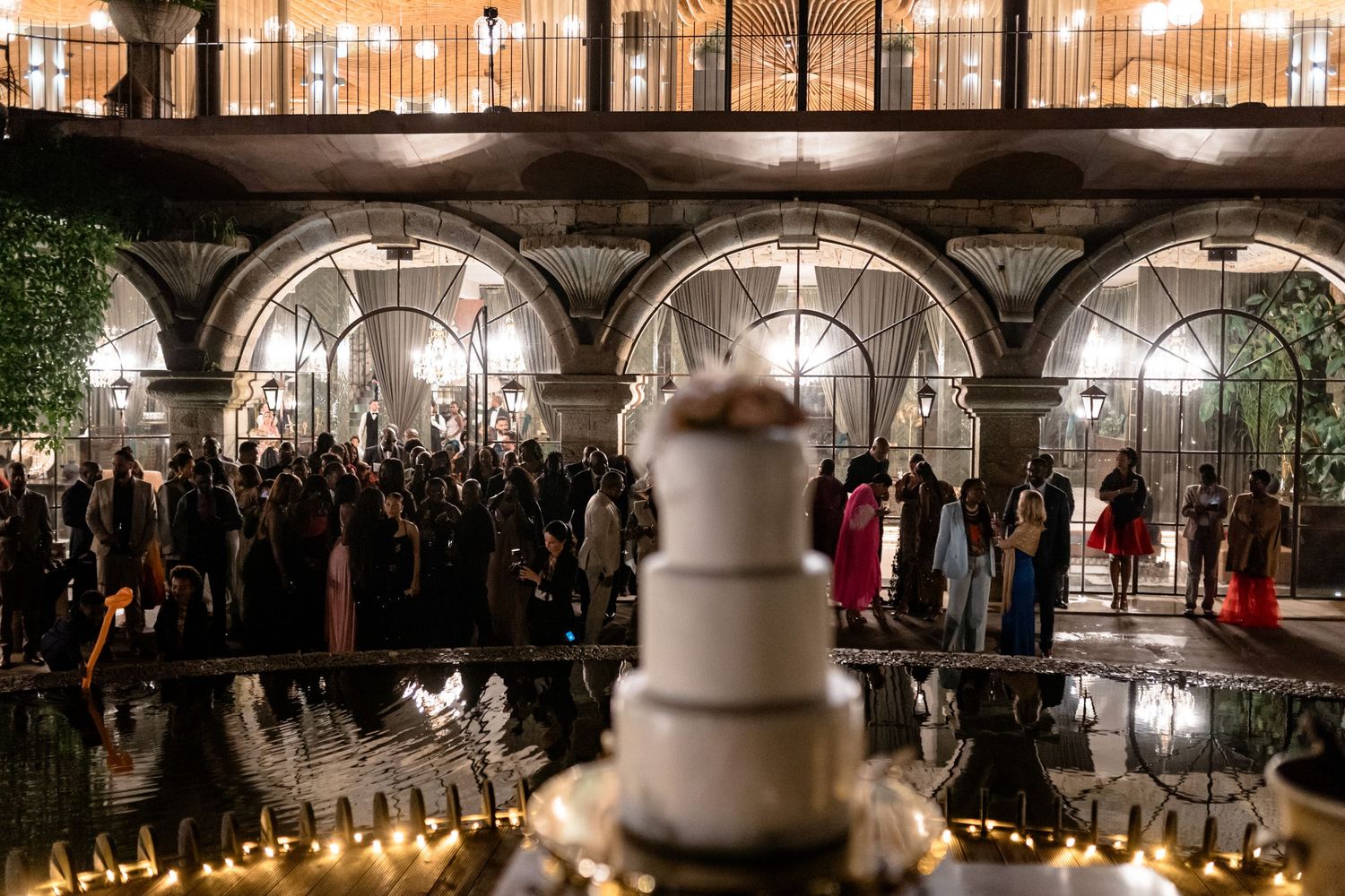 Panoramic view of an elegant ballroom reception with chandeliers and wedding cake.