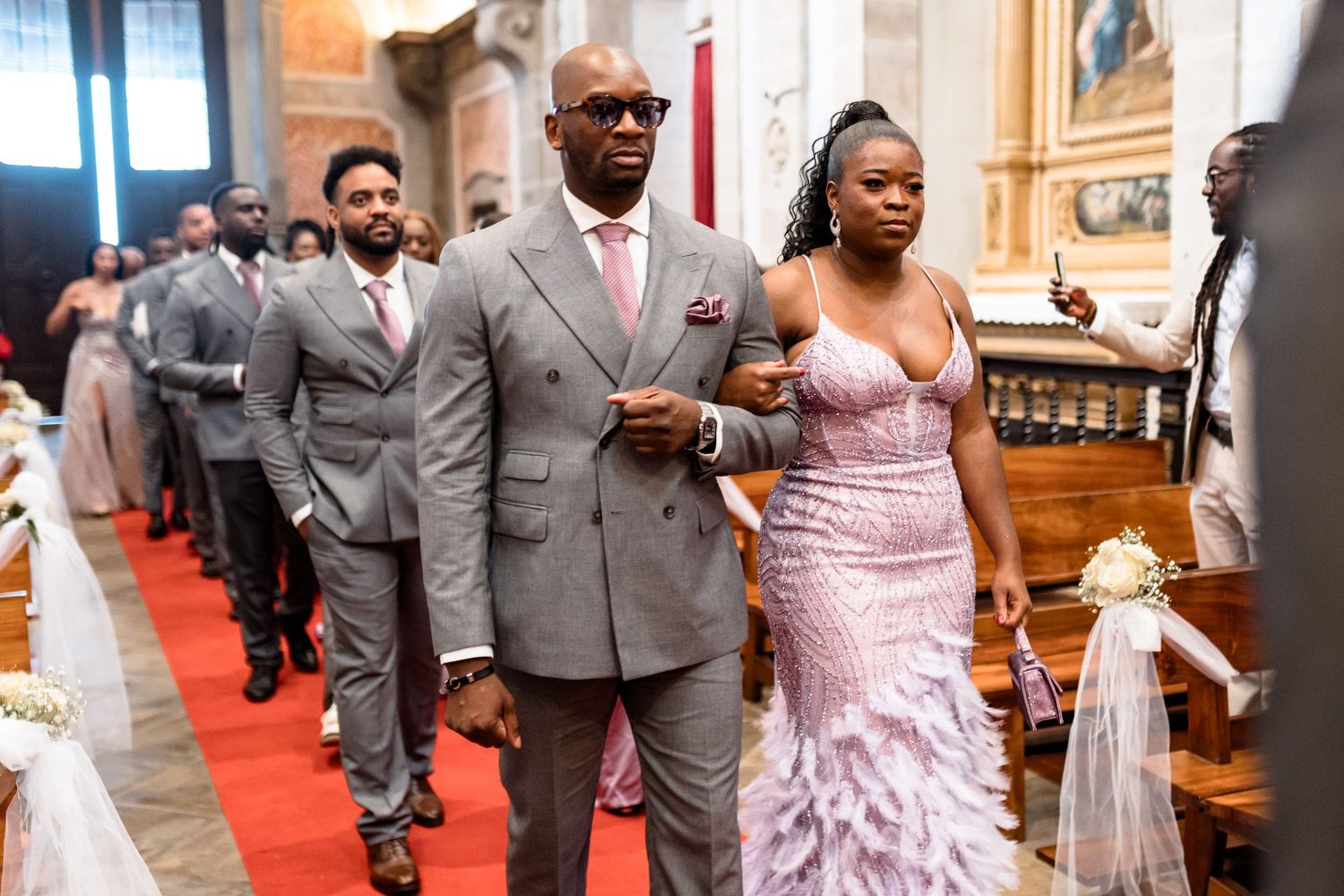 Wedding party processional in church with grey suits and pink gown.