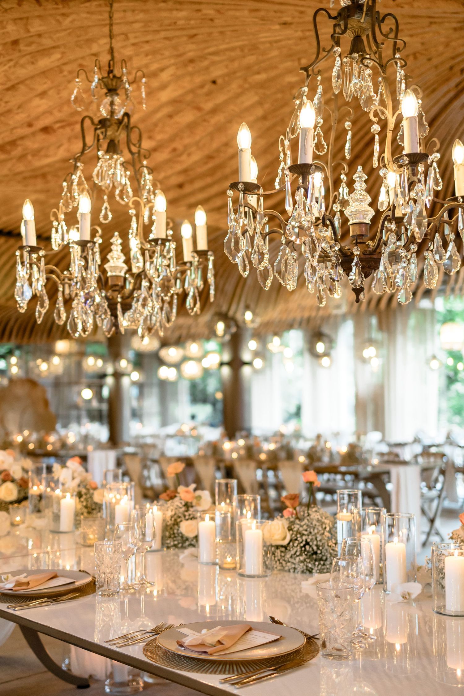 Crystal chandeliers hang above elegant table settings creating a romantic wedding reception atmosphere.