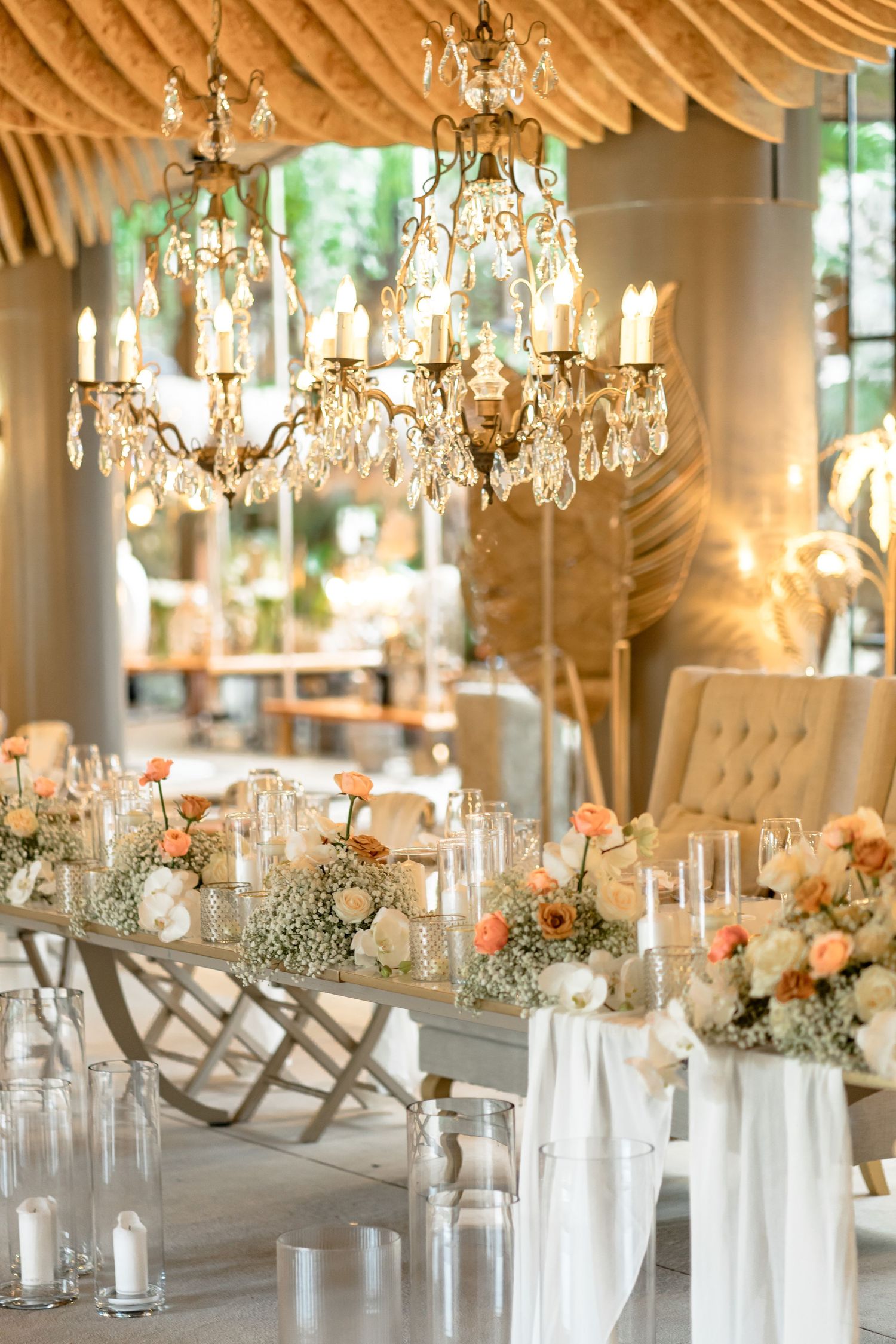 Elegant wedding reception table with crystal chandeliers and peach floral centerpieces.