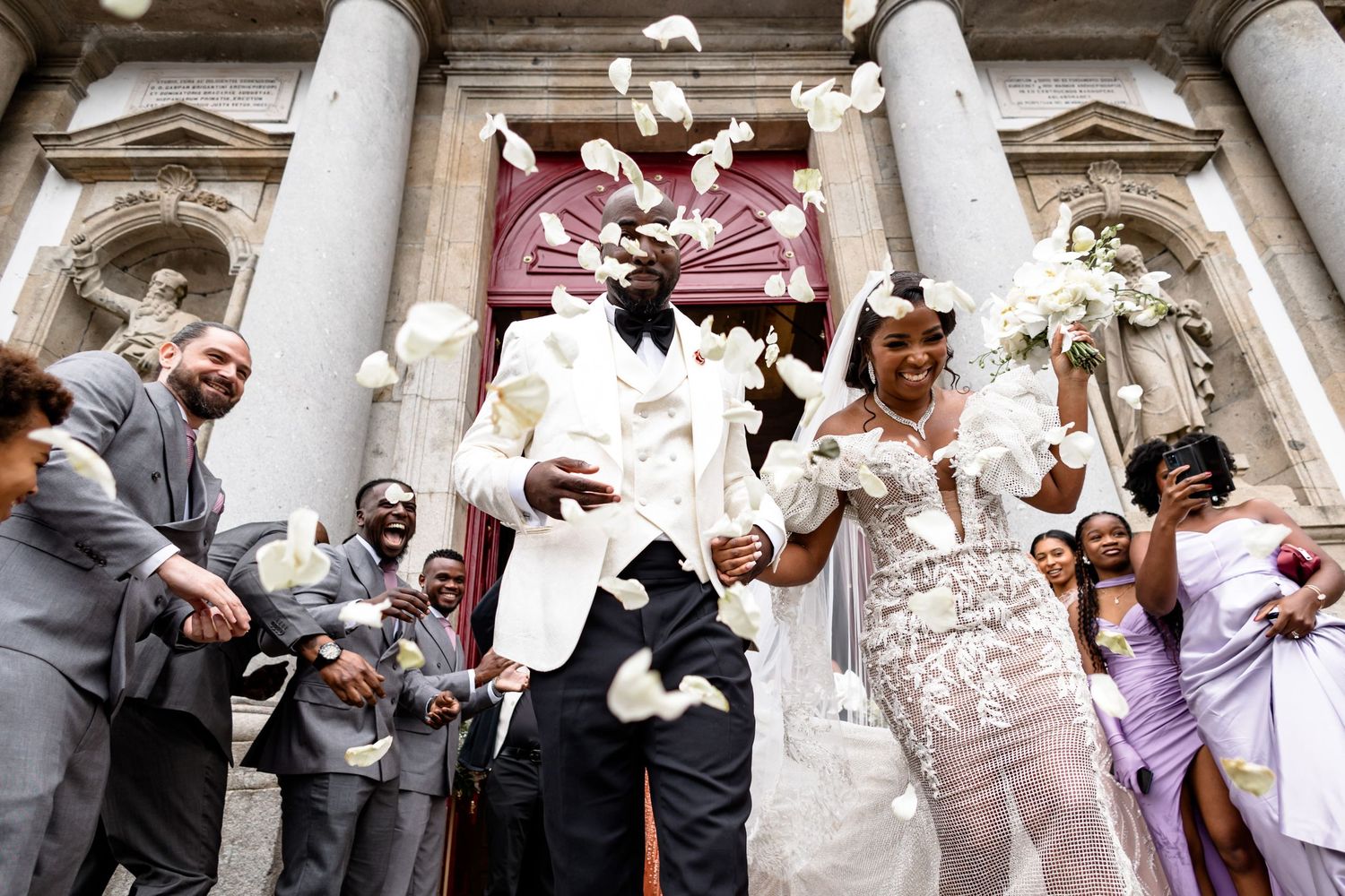 Wedding party celebrates under classical stone columns at an elegant venue.
