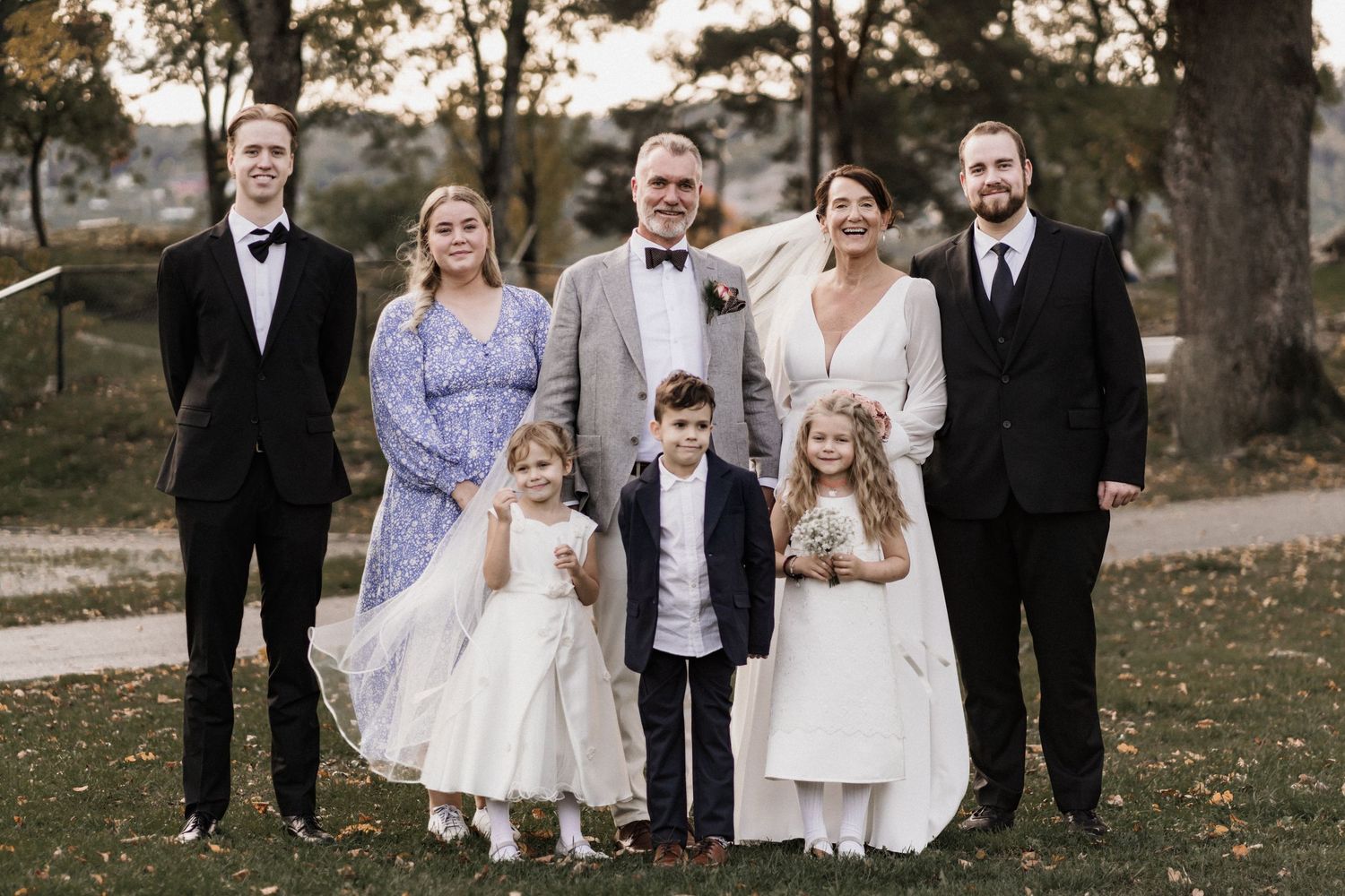 Wedding party in formal attire posing together outdoors in autumn setting.