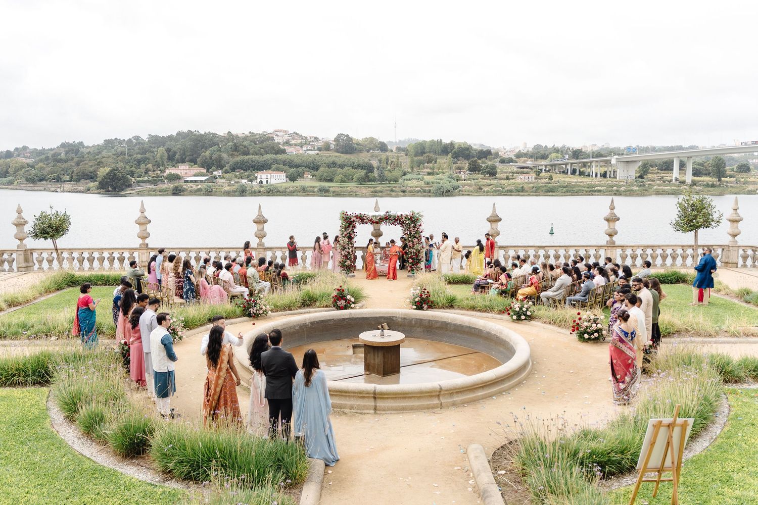 Outdoor wedding venue overlooking a waterfront with guests gathered in a circular arrangement.