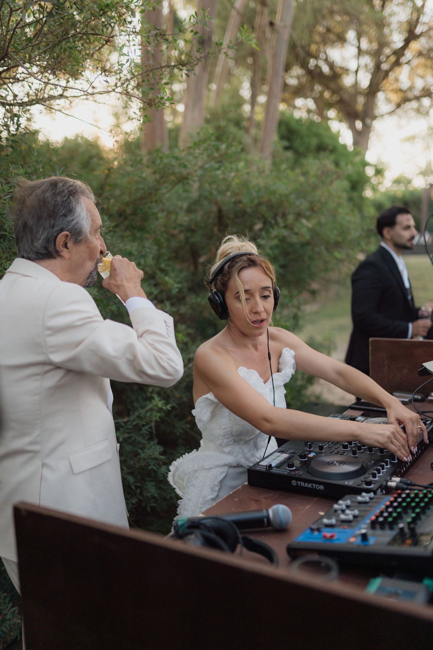 DJs working professional equipment at wooden booth during outdoor wedding.