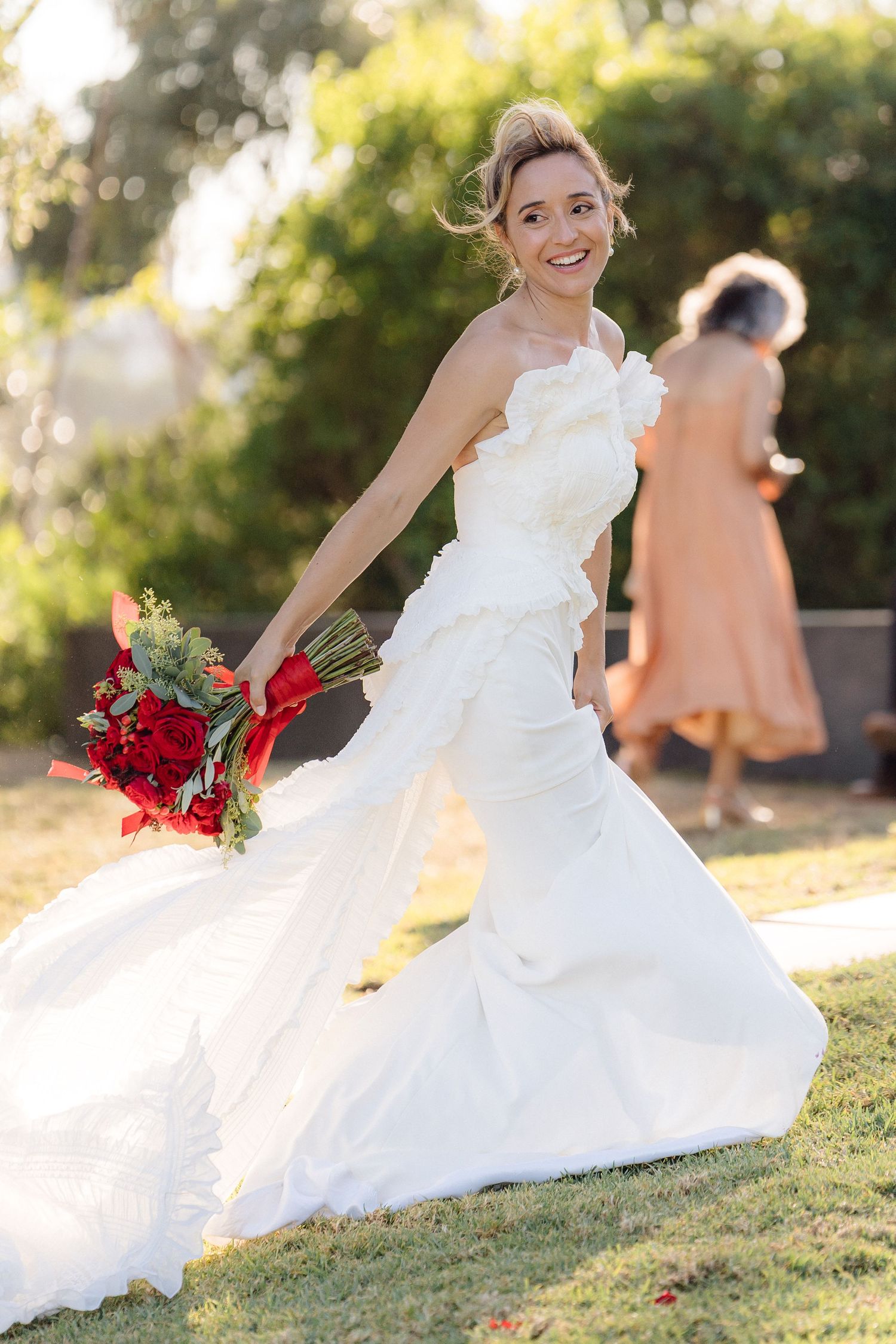 A bride in a flowing white dress twirls playfully on a grassy hill during golden hour.