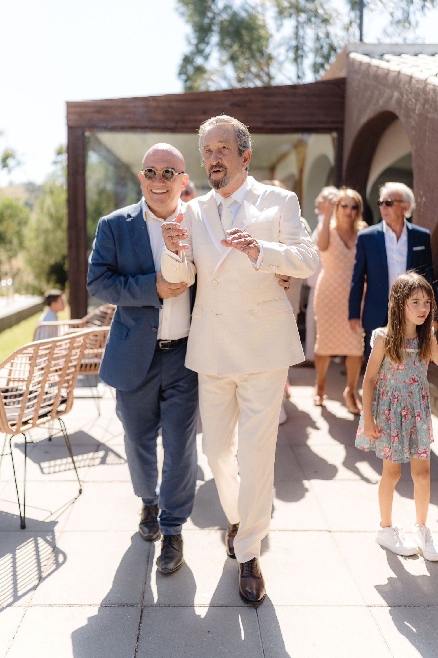 Wedding guests walking and mingling on outdoor patio with wooden chairs.