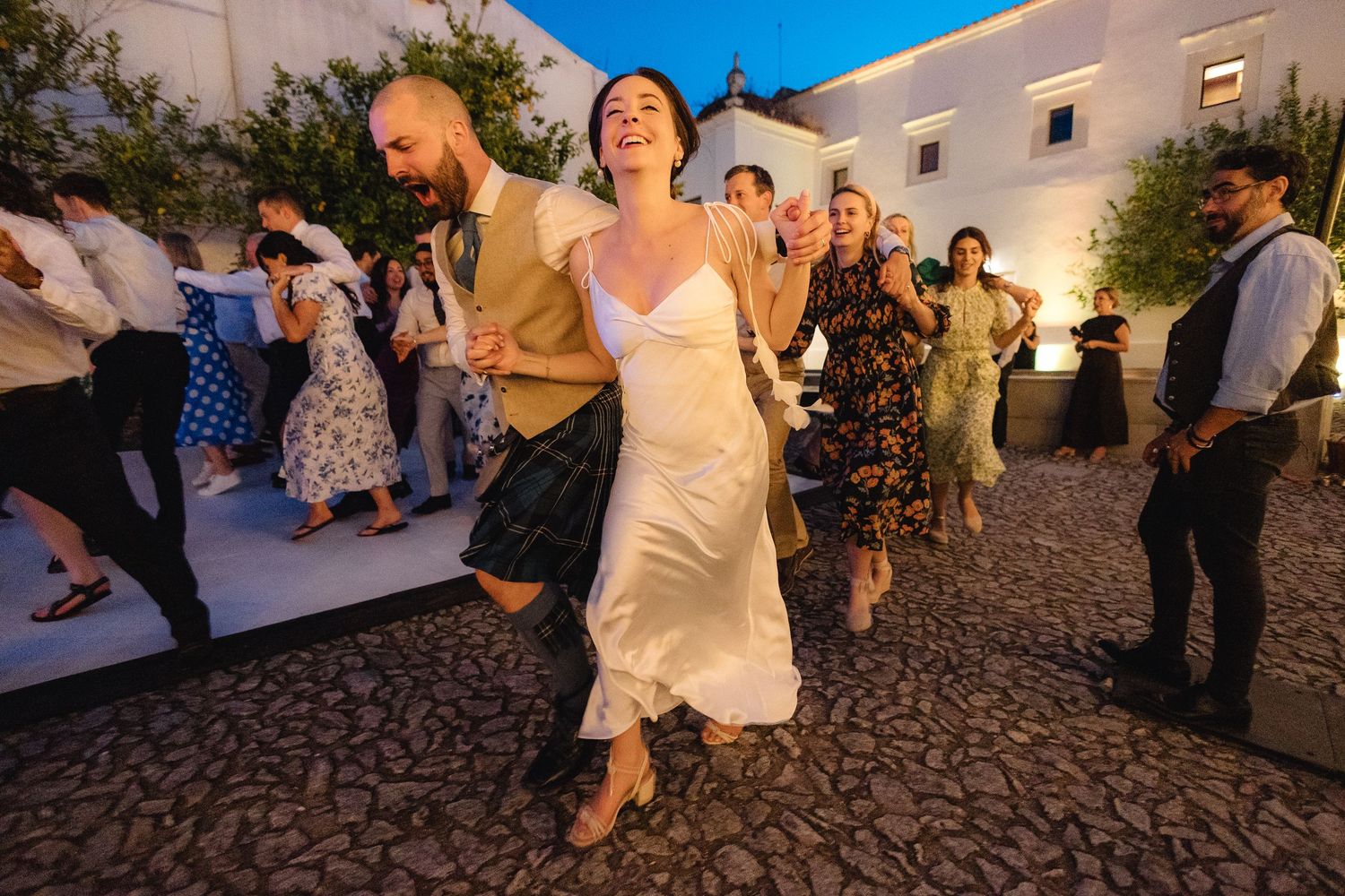 Wedding celebration on a cobblestone patio with white buildings in the background.
