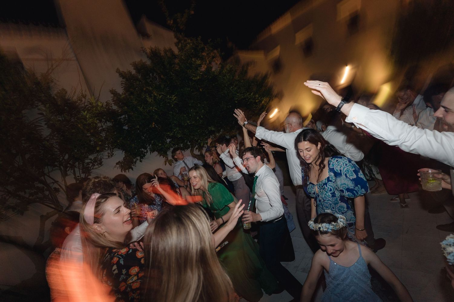 People with raised arms dancing energetically at a nighttime indoor party.
