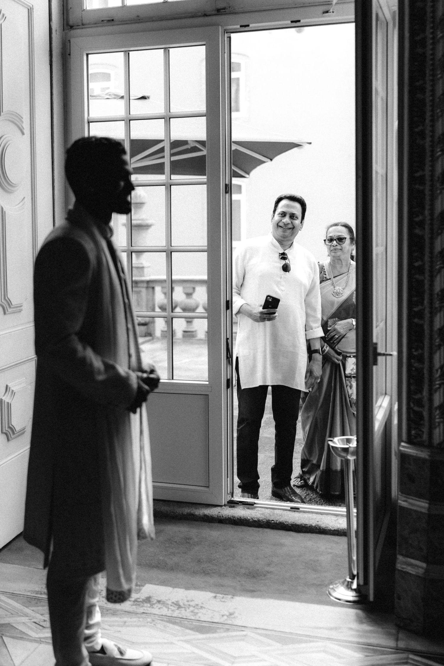 Black and white photo of people gathering near windows in an interior space.